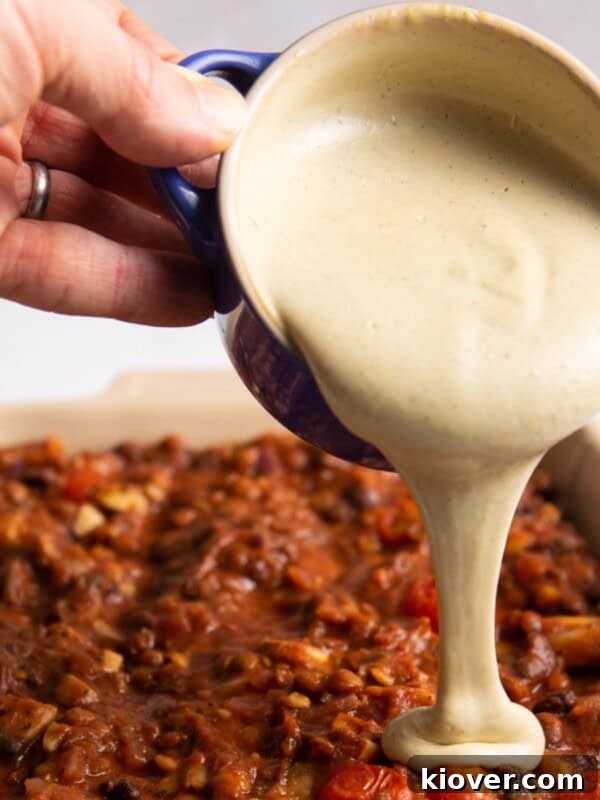 Creamy Vegan Tzatziki Sauce Recipe for Mediterranean Dishes 9 white sauce being poured onto of lasagne.