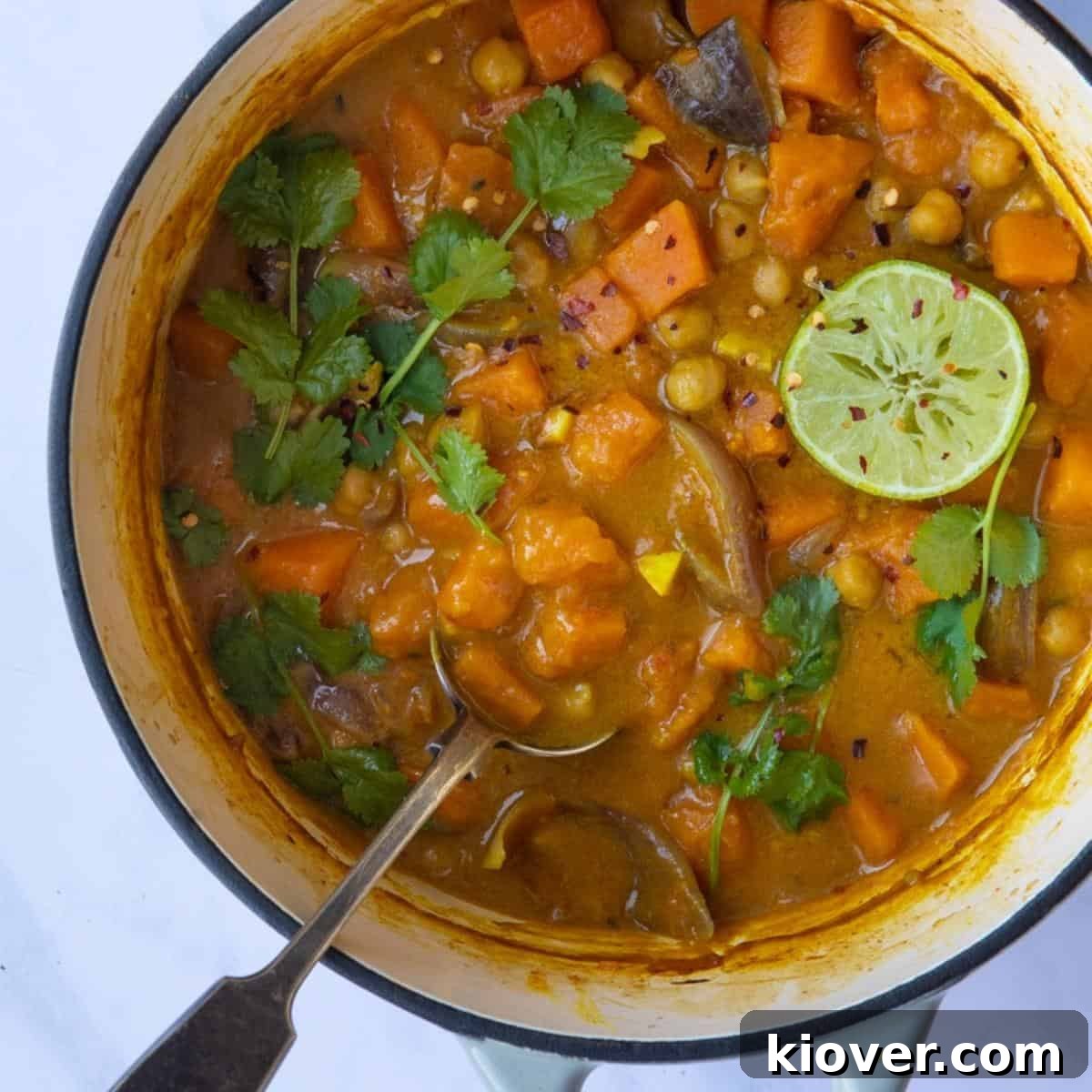 Sweet Potato Satay Curry served cooking pot, topped with coriander and lime wedges. Pot is displayed on a white marble background.
