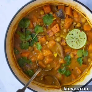 Sweet Potato Satay Curry displayed in a large pot with serving spoon. Pot is displayed on white marble background