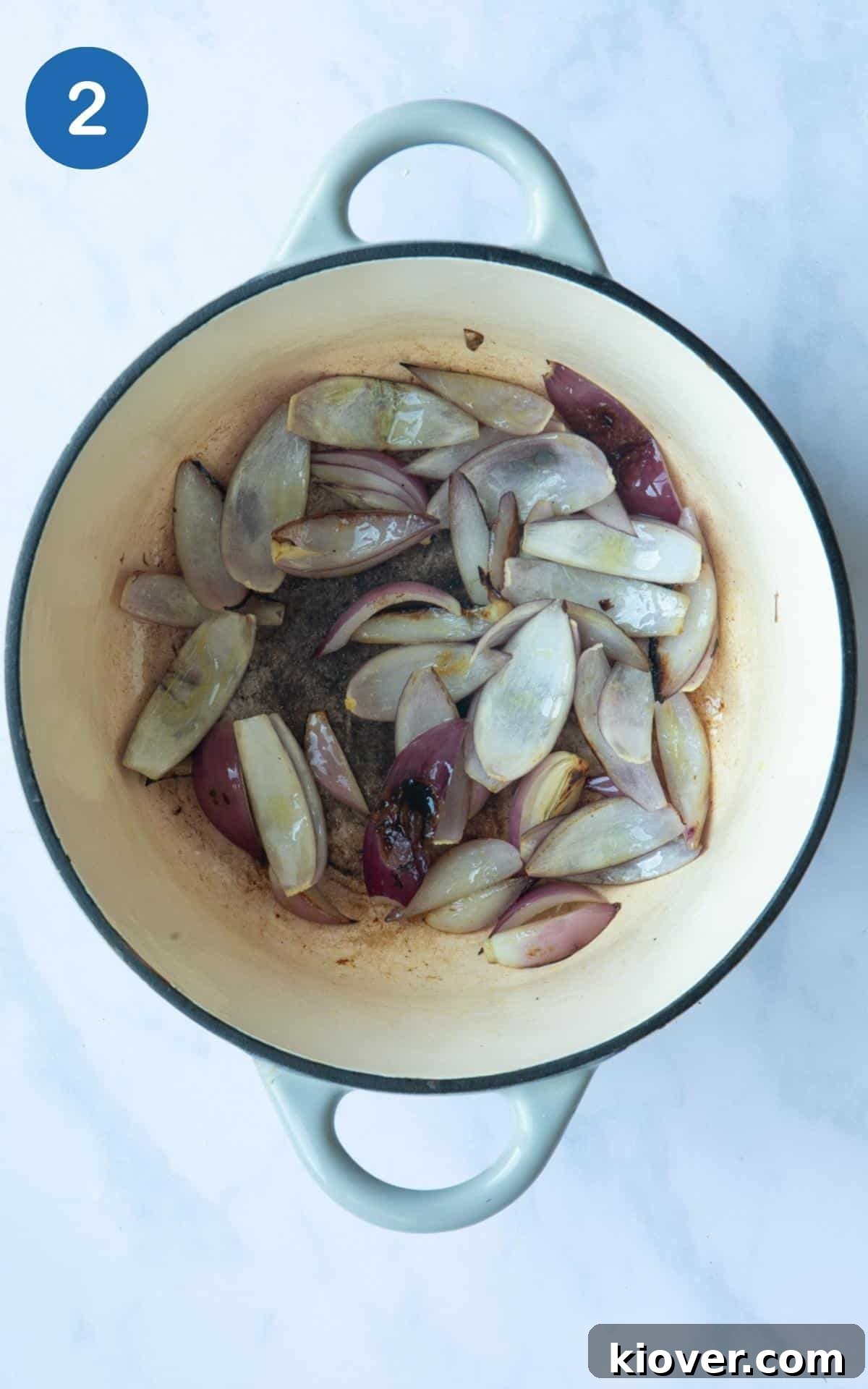 Chopped onions in a large pot, that have been cooked until they have slightly browned/charred. Displayed on a white marble background.