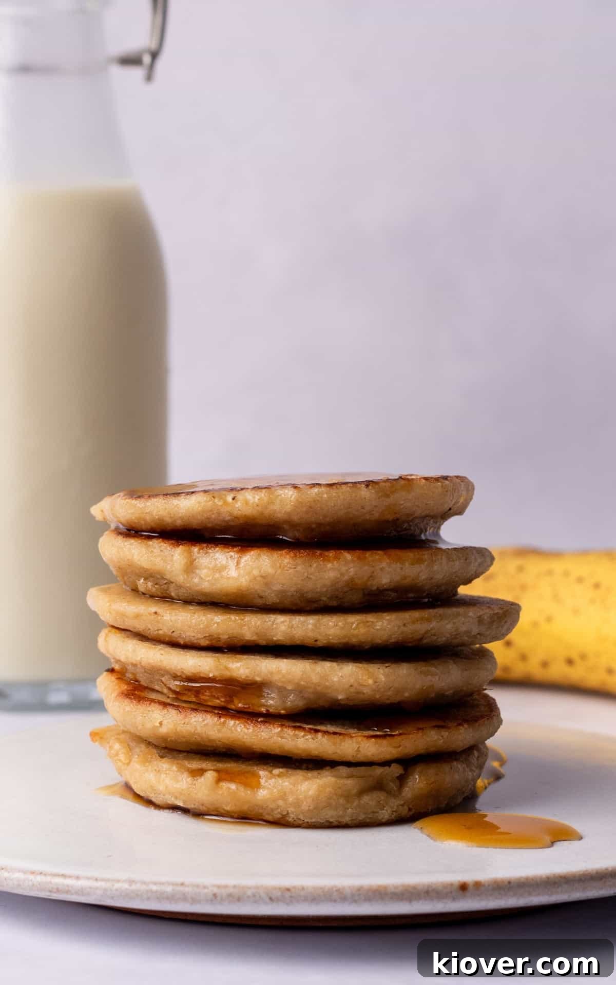 Fluffy Banana Oat Pancakes Recipe for Quick Morning Meals 7 Banana Oat Pancakes stacked on a plate with a bottle of milk and banana in the backround.