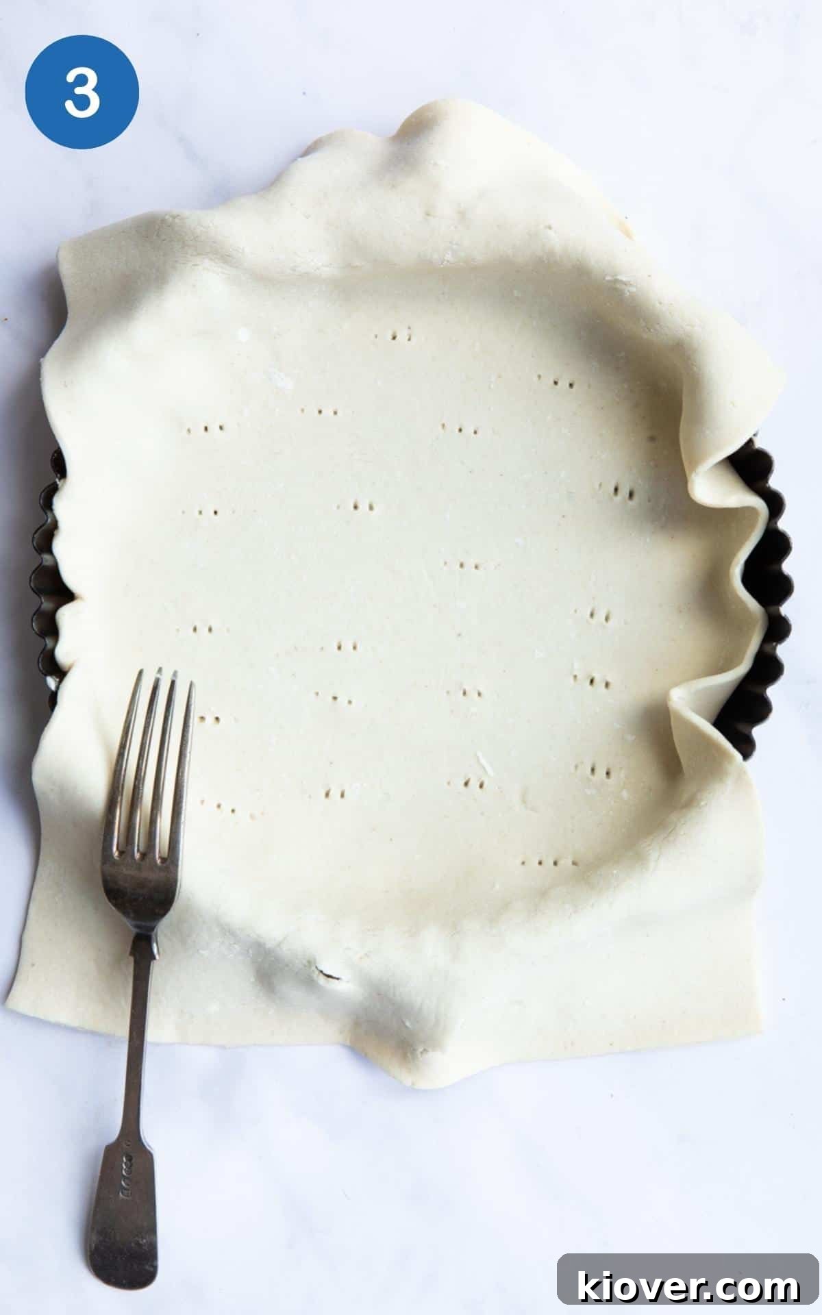 Sheet of pastry laid over a circular fluted tin with fork pricks in it.