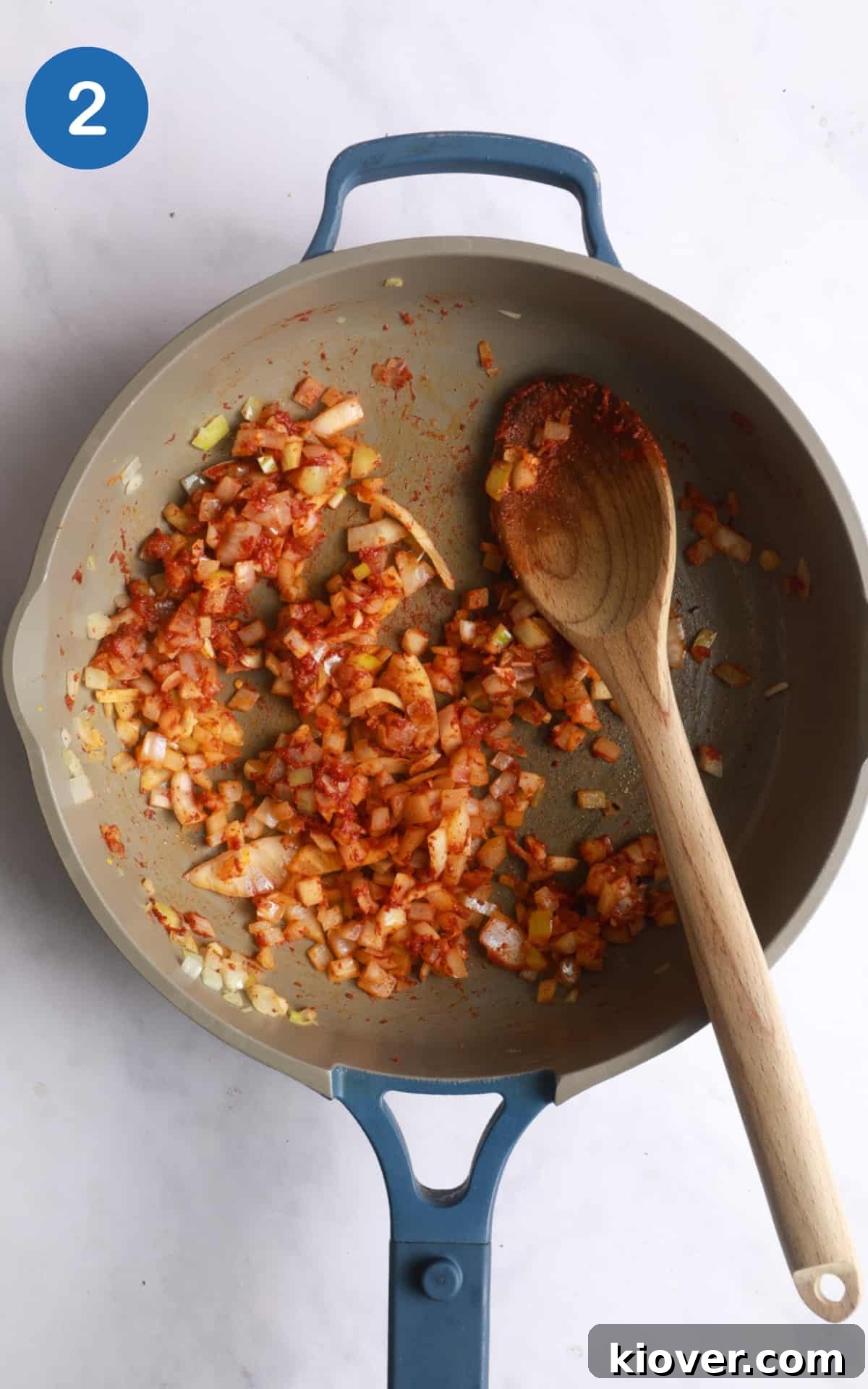 Onions being fried with spices and tomato puree on white marble background.