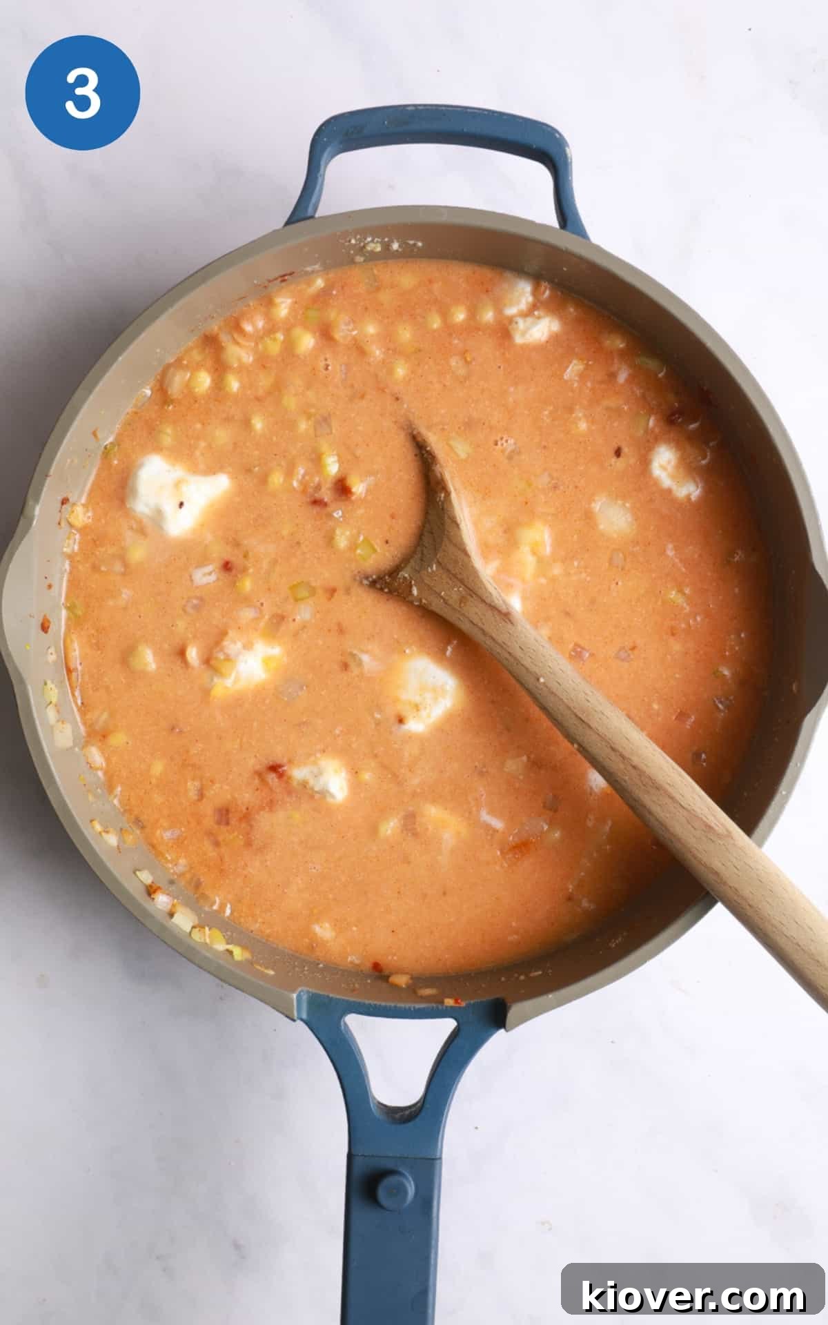 overhead shot of chickpea curry with wooden spoon in large frying pan. Pan is on white marble background.