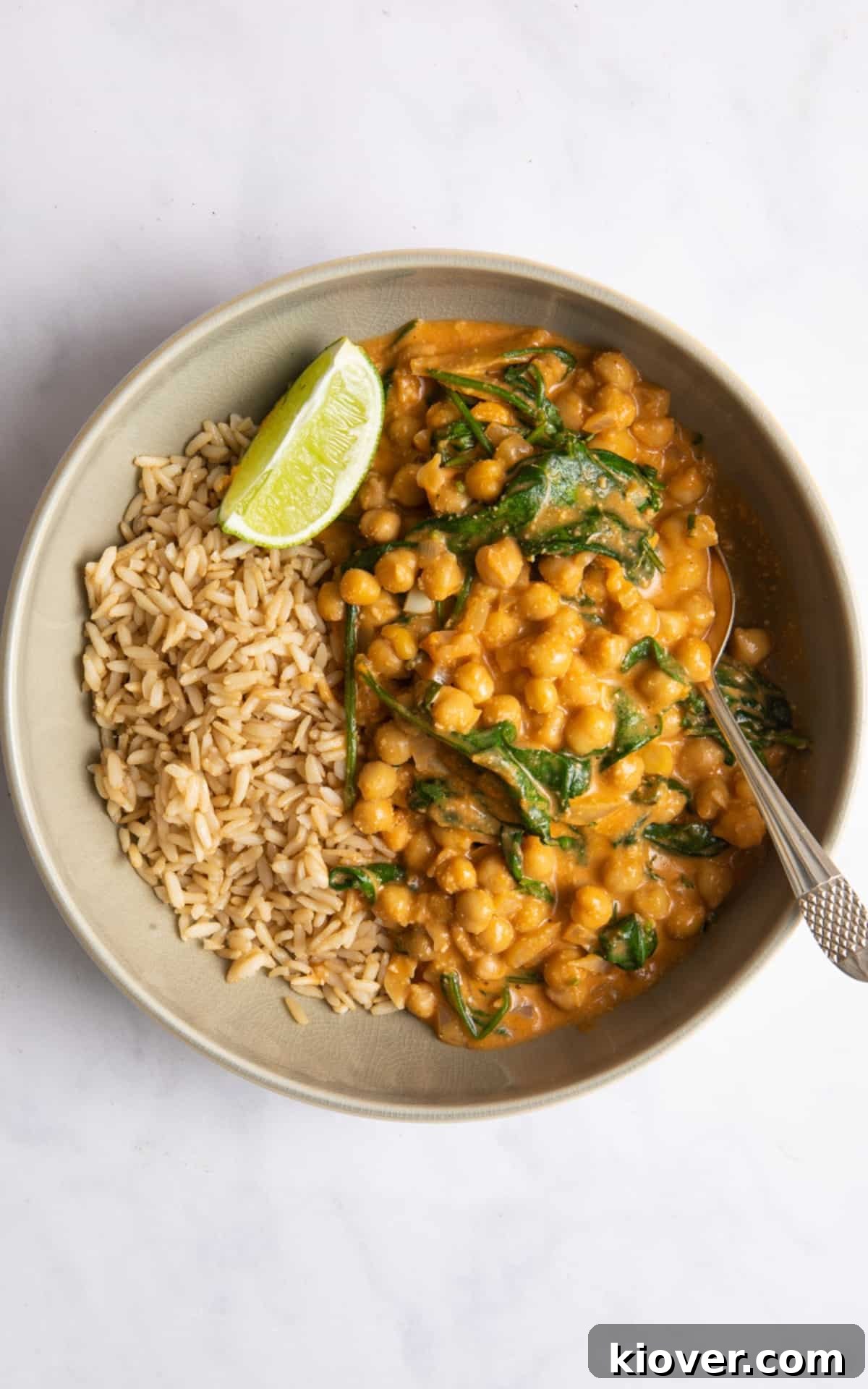 chickpea curry in beige bowl with brown rice and fresh lime wedge.