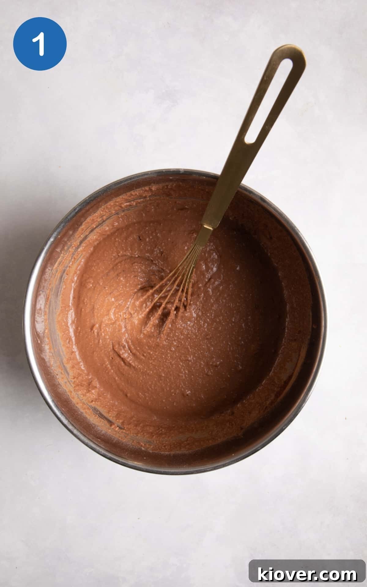 chocolate cake mixture in silver mixing bowl with whisk on white background.