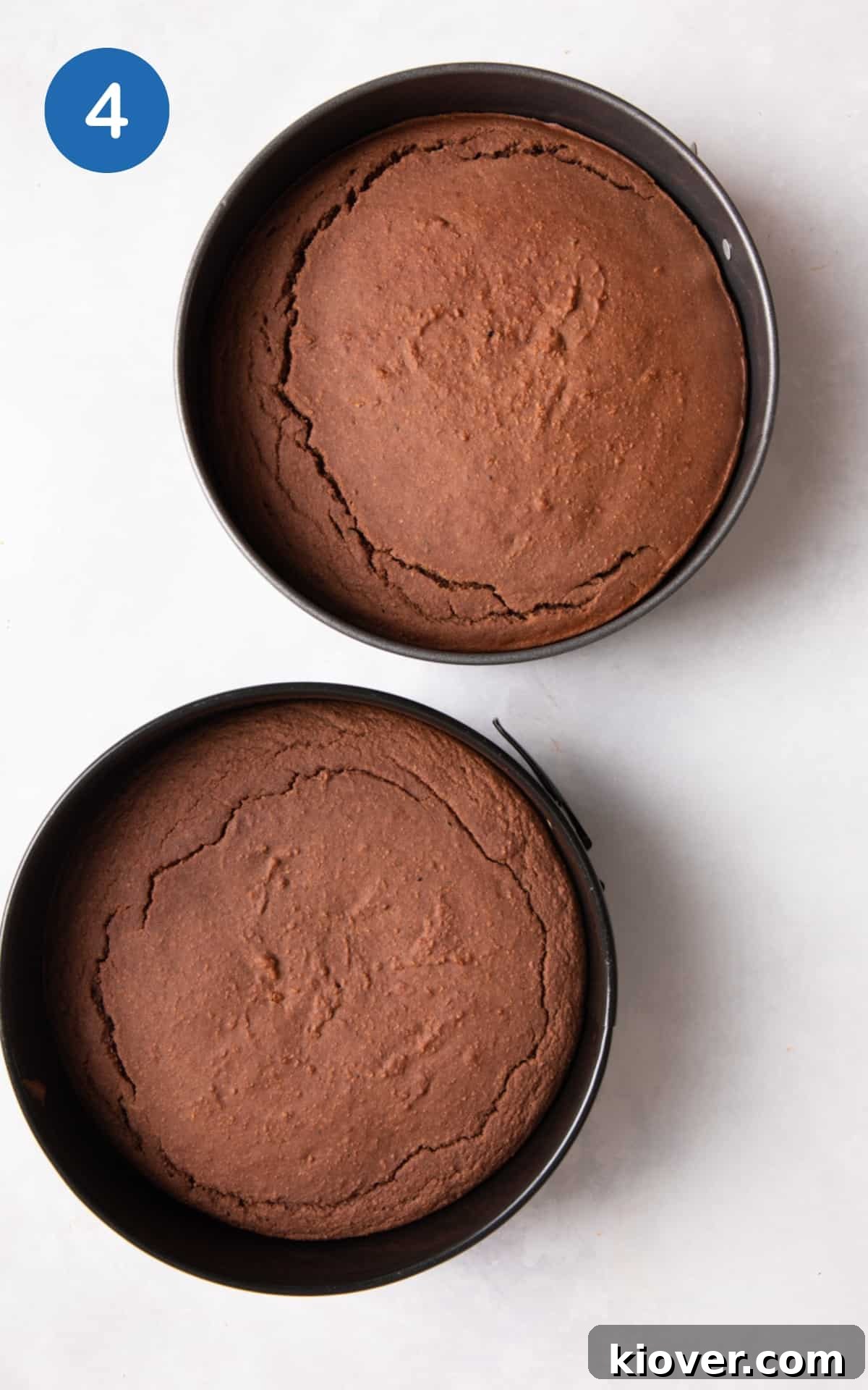 2 baked chocolate cakes in cake tines on white surface.
