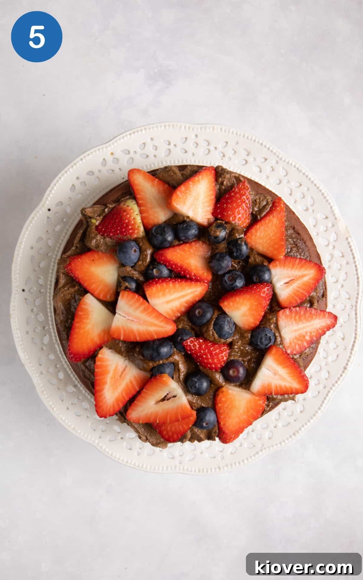 overhead shot of cakes on cake stand topped with fresh berries on white surface.