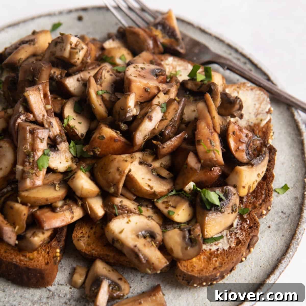 Garlic Butter Mushrooms on Toast with Herbs 2 garlic mushrooms on toast on grey plate with fork.