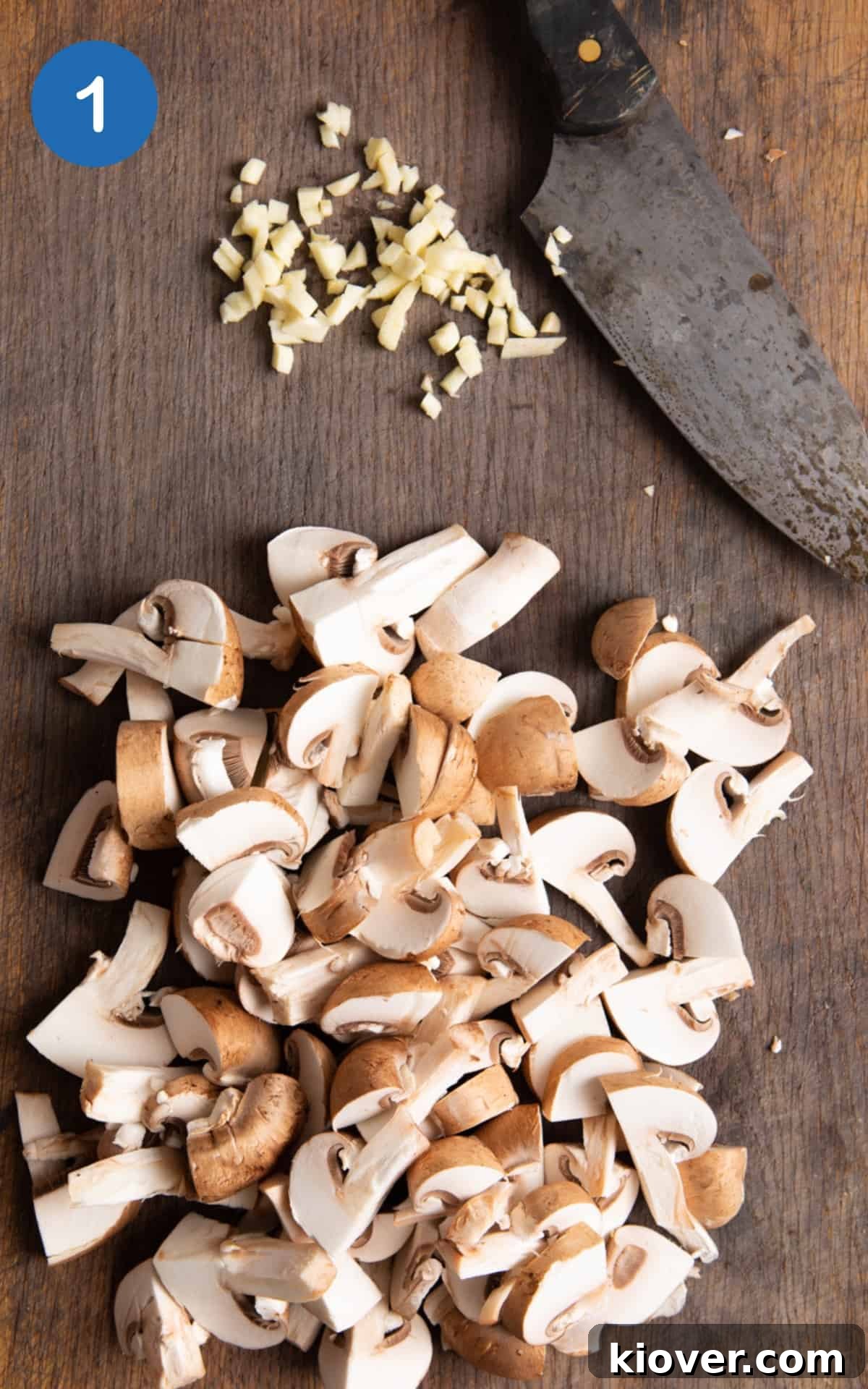 Garlic Butter Mushrooms on Toast with Herbs 4 chopped mushrooms and garlic on dark wooden chopping board with sharp knife.