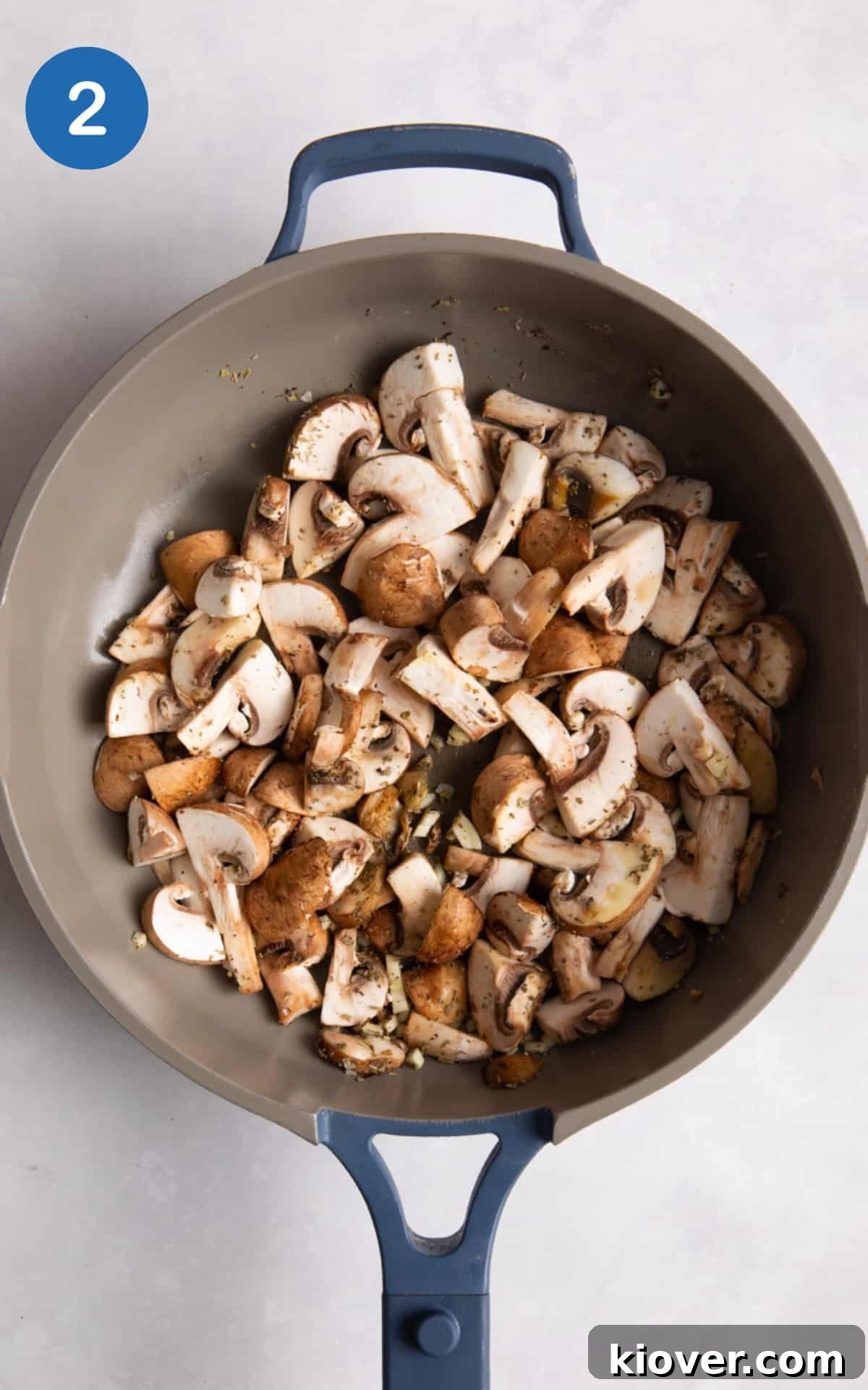 Garlic Butter Mushrooms on Toast with Herbs 5 mushrooms in blue frying pan on white surface.