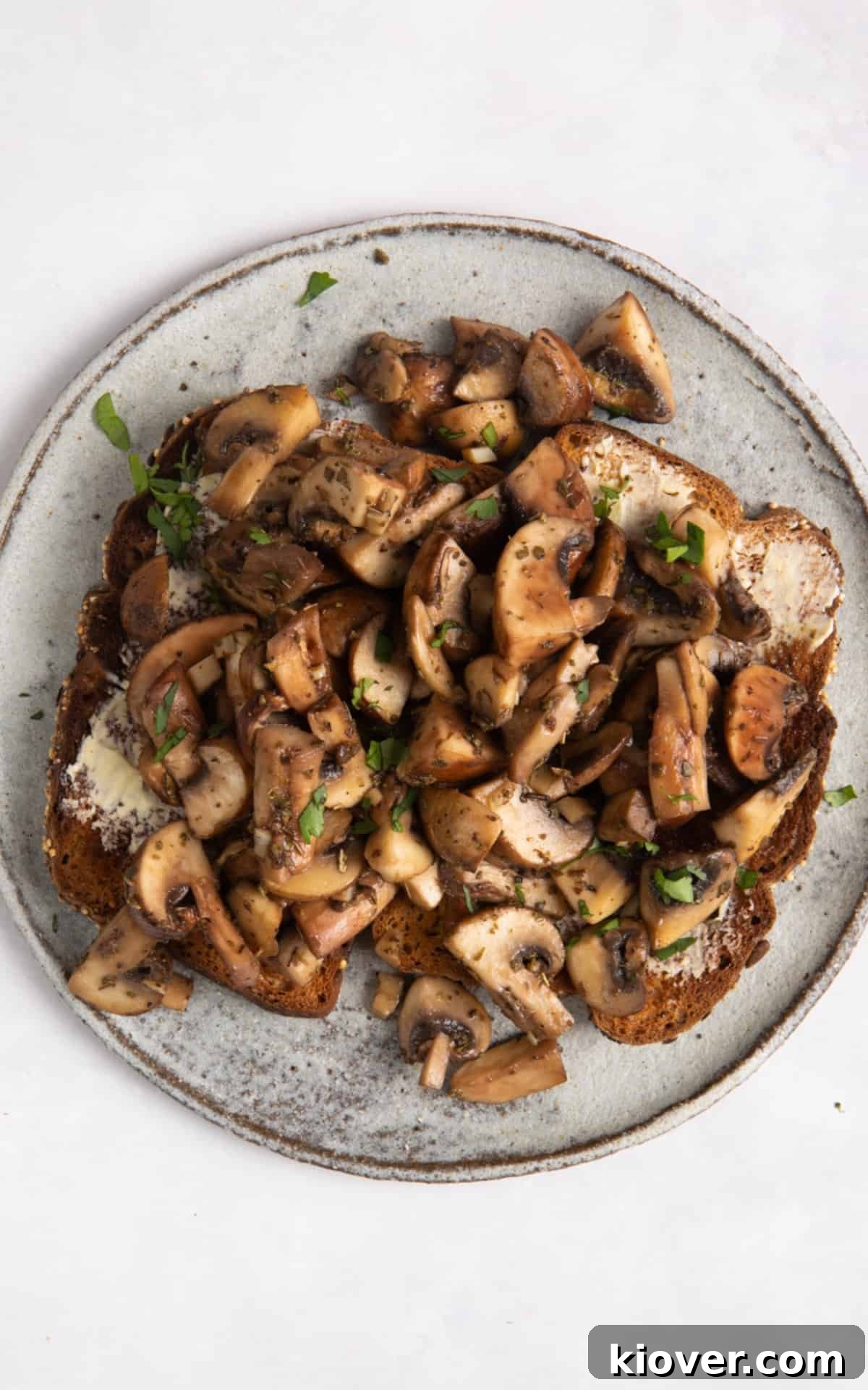 Garlic Butter Mushrooms on Toast with Herbs 7 overhead shot of garlic mushrooms on toast on grey plate. Plate Is on white surface.