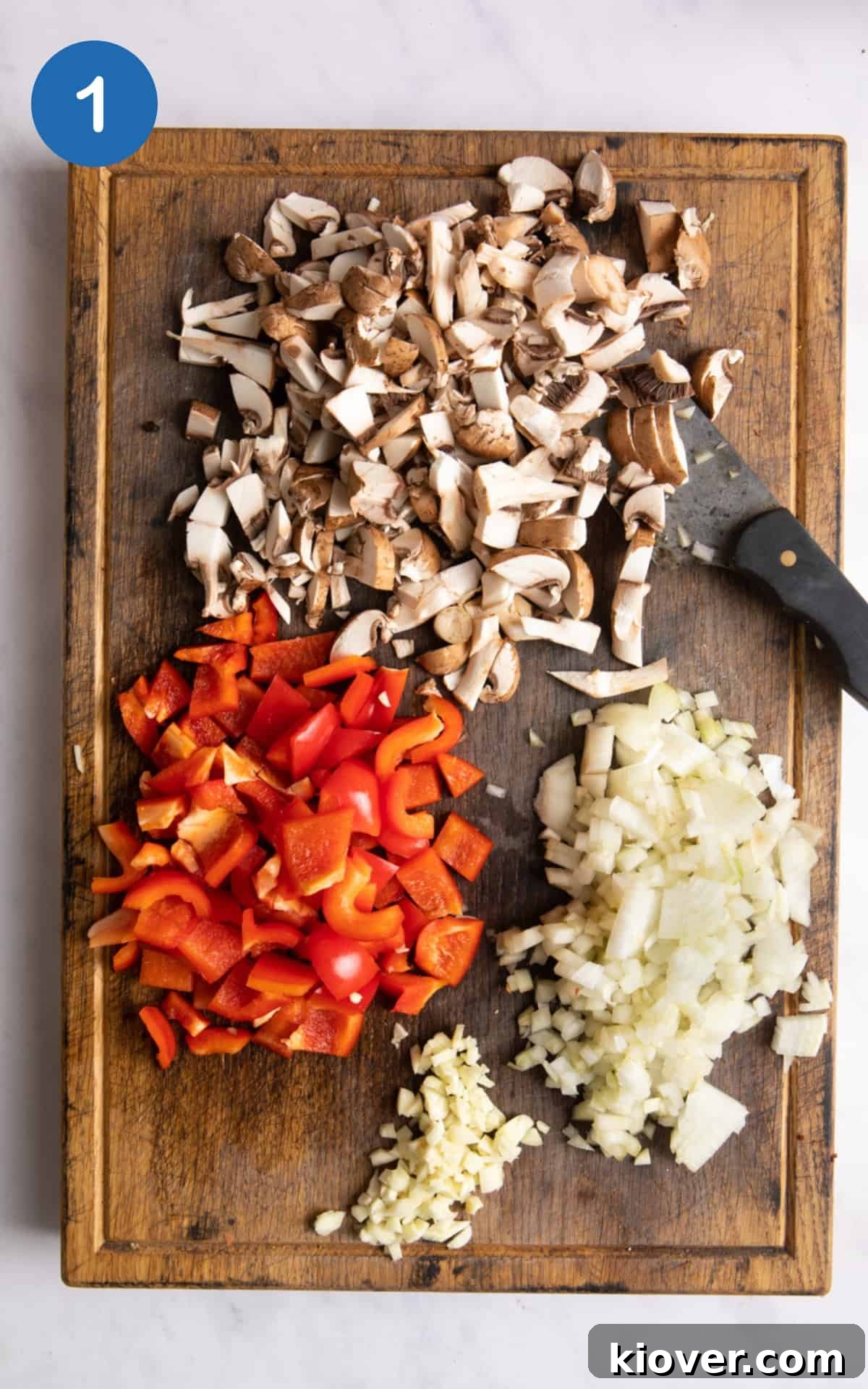 Slow Cooker Vegan Chili Recipe for Busy Weeknights 4 mushrooms, peppers, onion and garlic chopped on a dark wooden chopping board with knife.