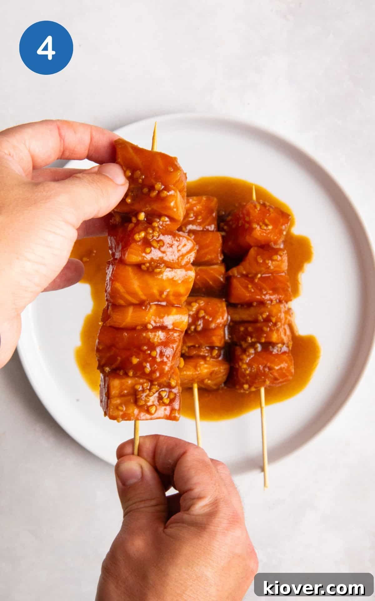 Two hands holding skewers with salmon cubes.