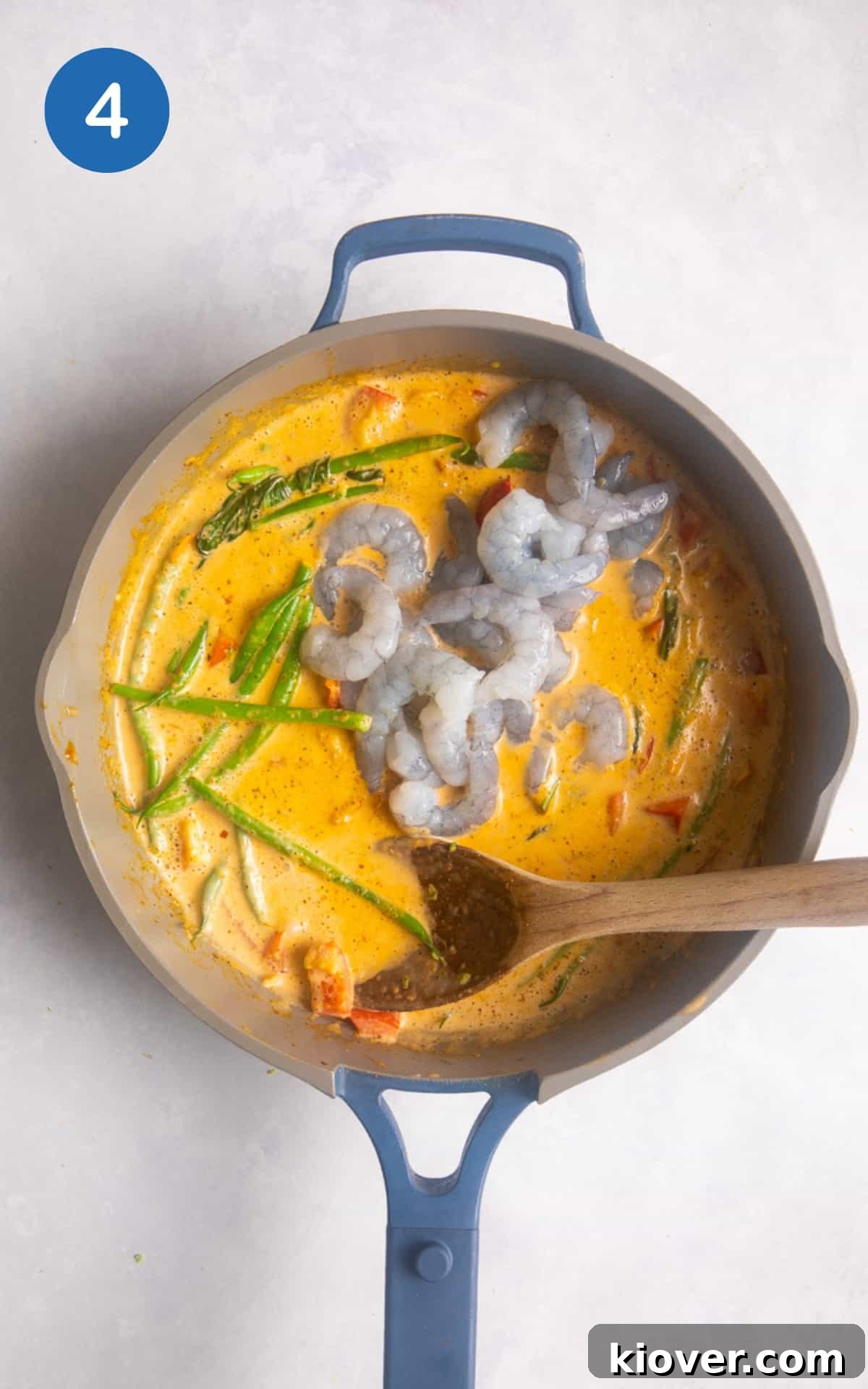 prawns added curry in large shallow frying pan on white surface.
