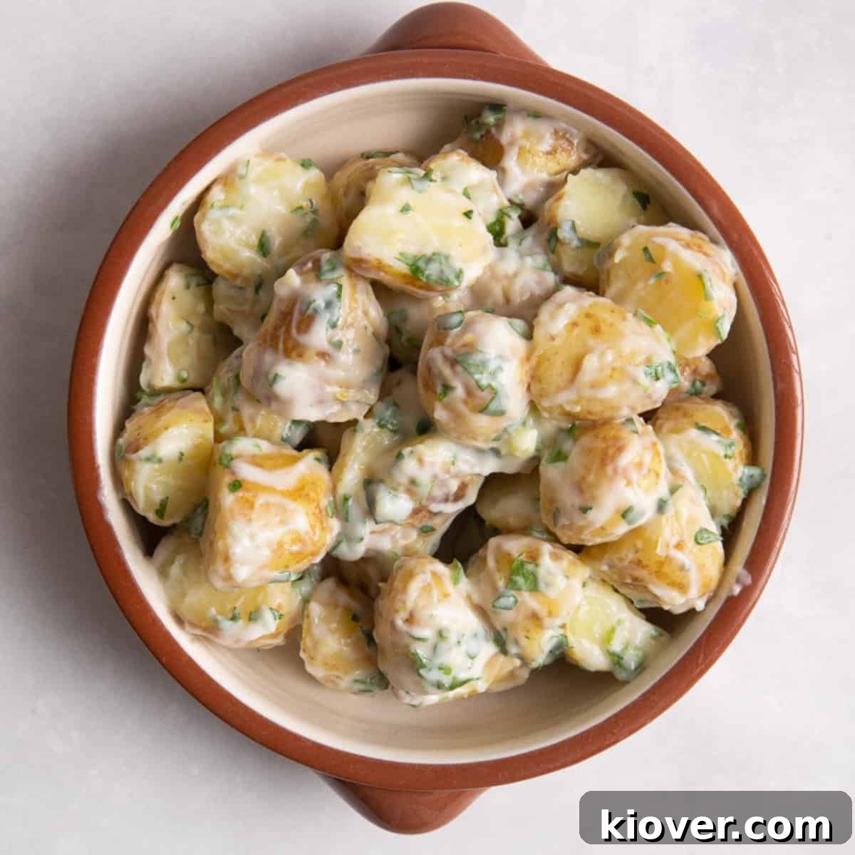 Creamy Yogurt Potato Salad with Fresh Herbs 2 overhead shot of potato salad in brown/orange bowl on white surface.
