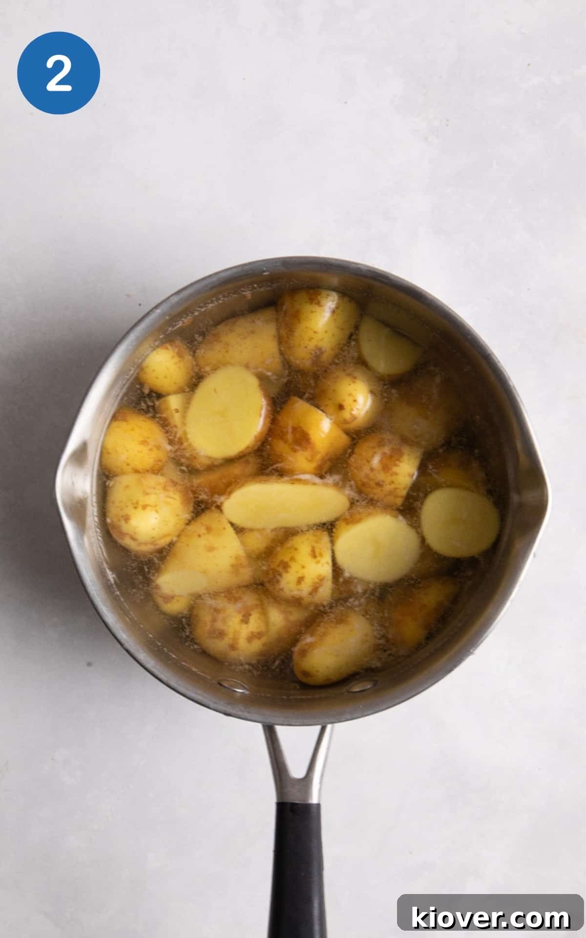 Creamy Yogurt Potato Salad with Fresh Herbs 5 new potatoes in large saucepan with water on white surface.