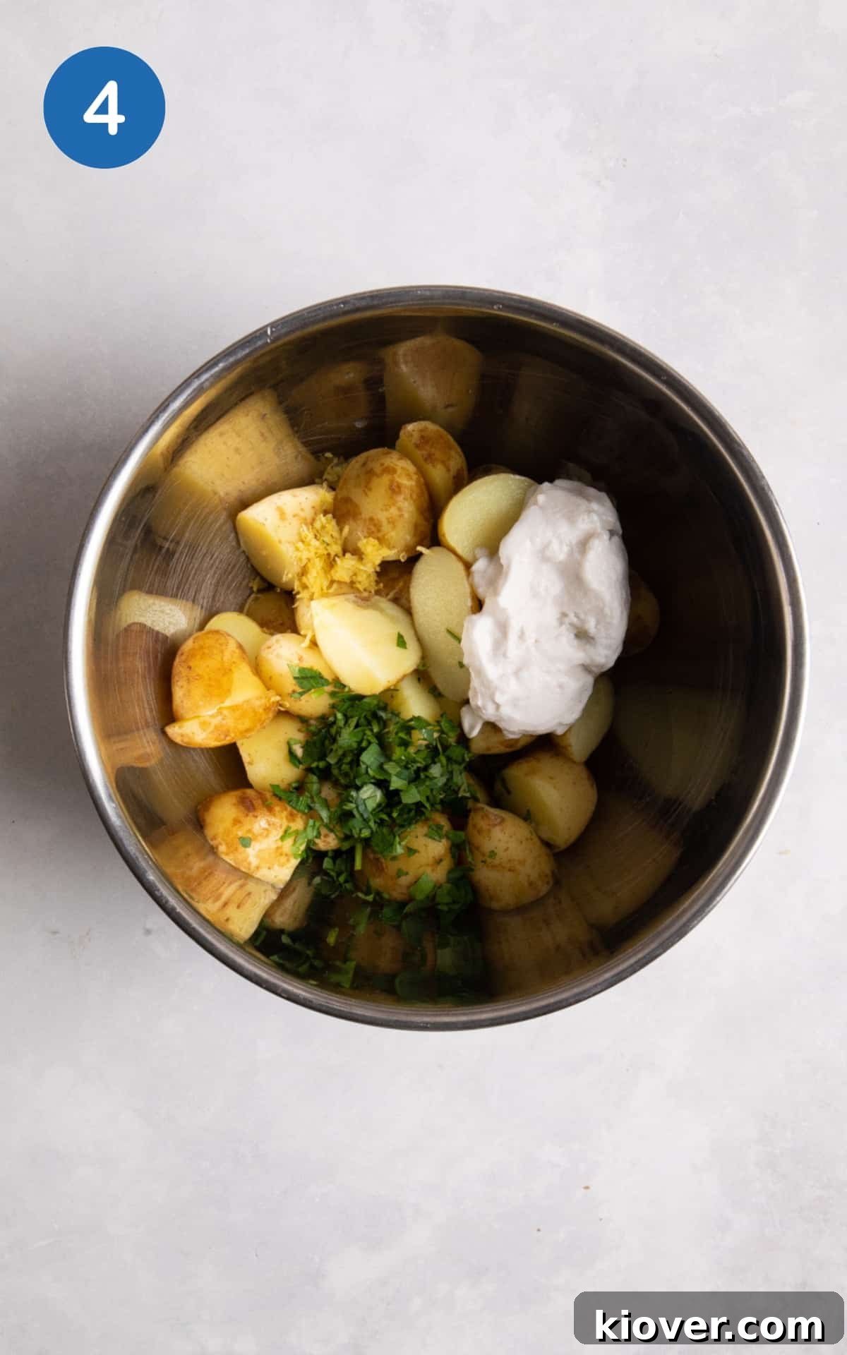 Creamy Yogurt Potato Salad with Fresh Herbs 7 new potatoes with yoghurt, parsley and lime zest in large silver mixing bowl. Mixing bowl is on white surface.