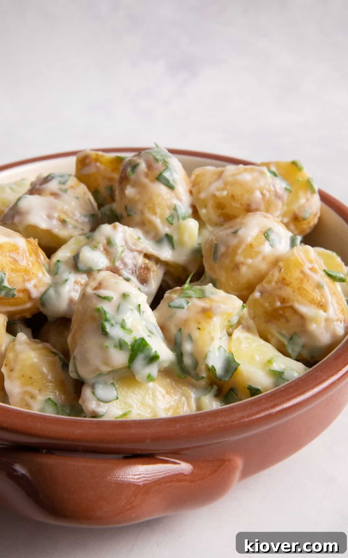 Creamy Yogurt Potato Salad with Fresh Herbs 9 Potato salad in orange bowl on white surface.
