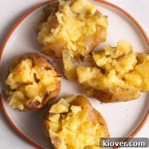 4 jacket potatoes cut open on a plate with melted butter on top.