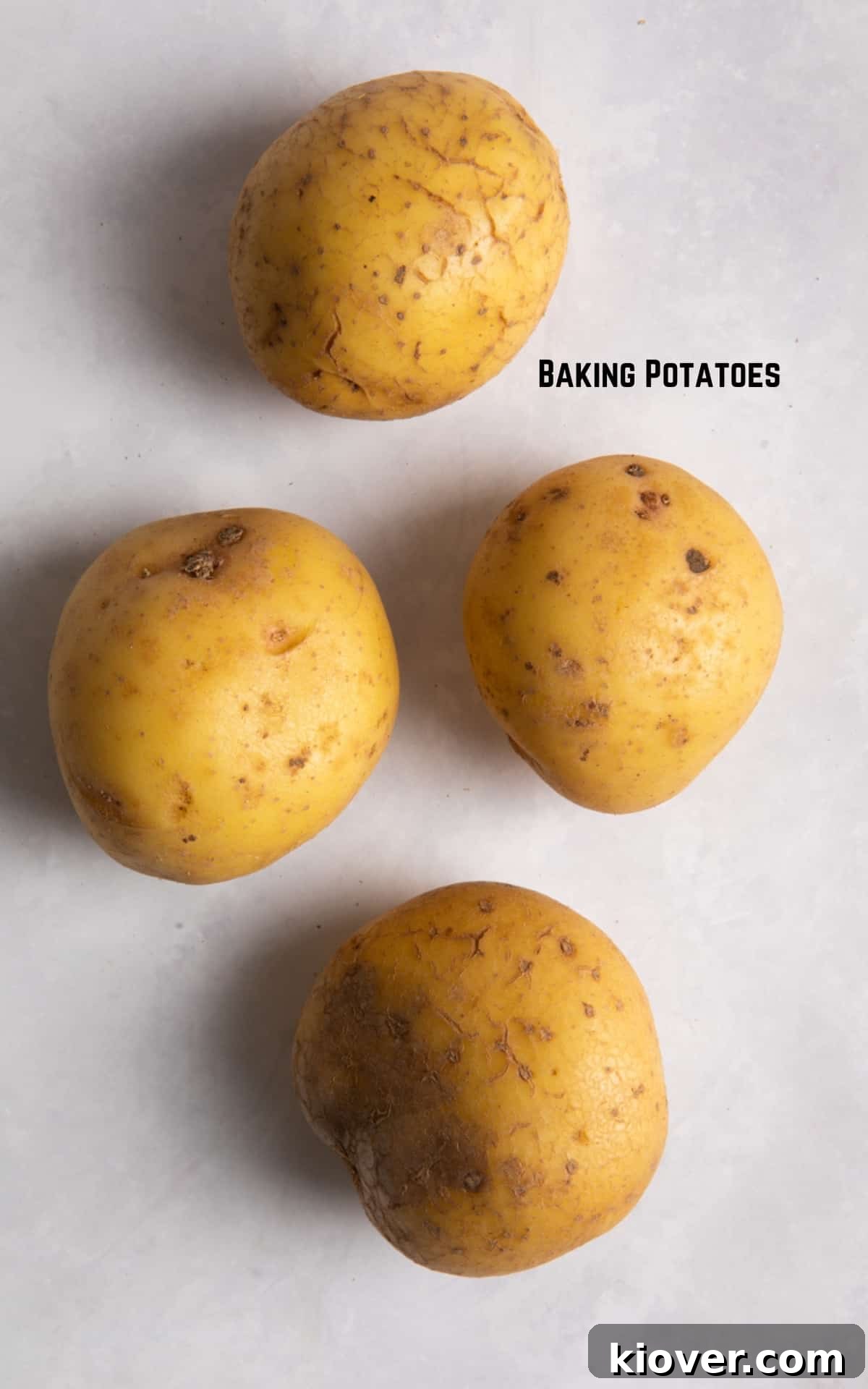 4 baking potatoes sat on a white marble background.