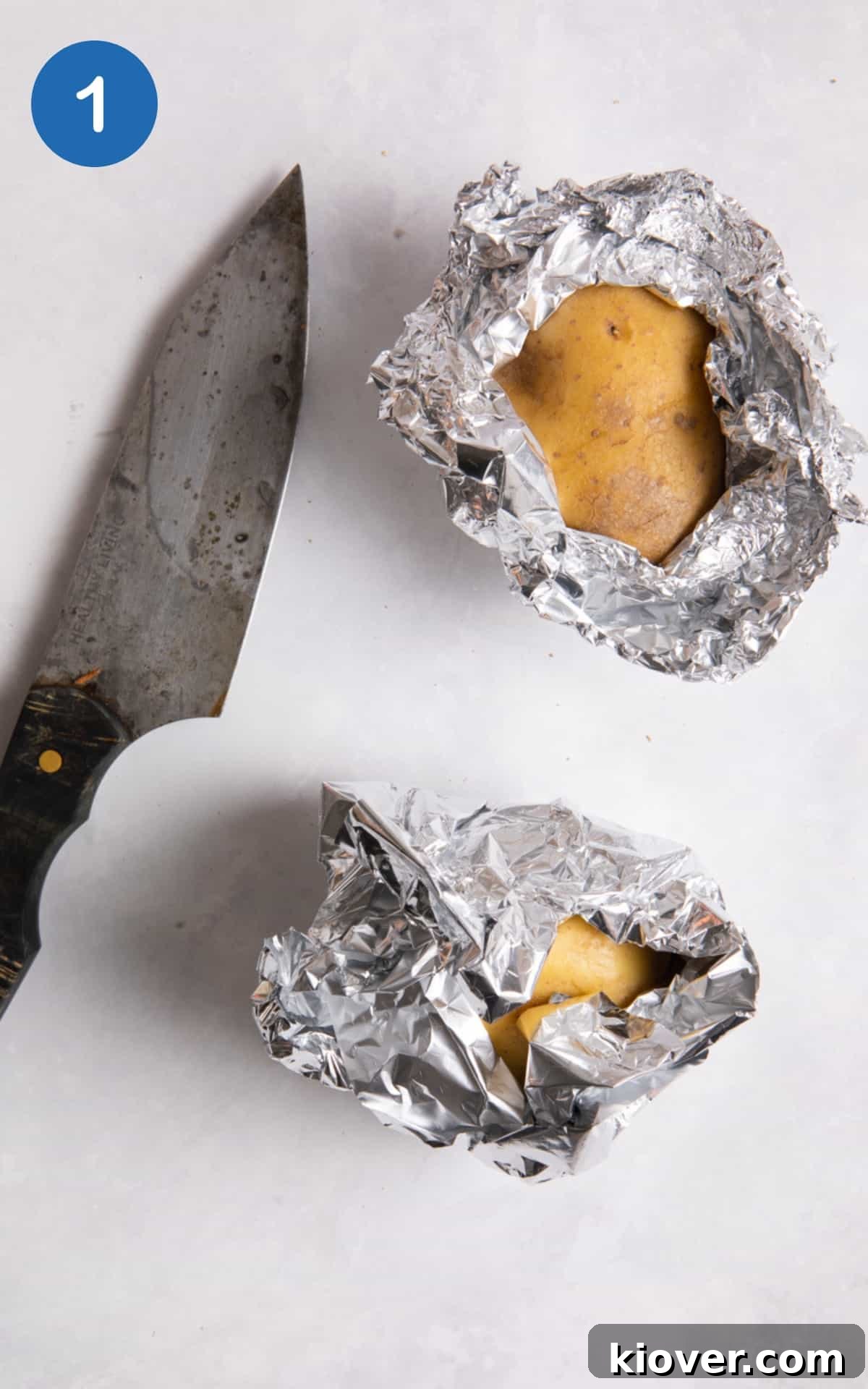jacket potatoes wrapped in tin foil with a knife on a white background.