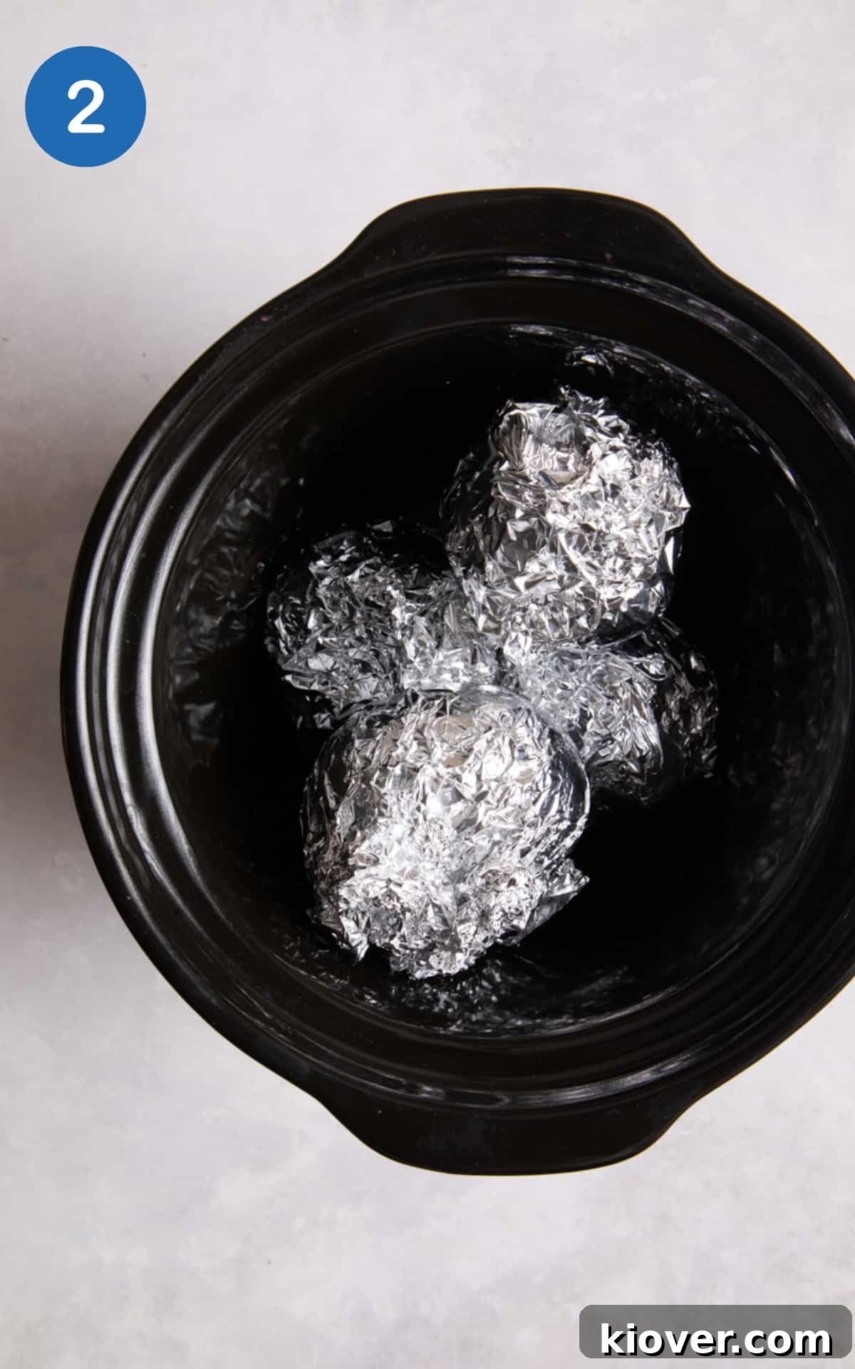 4 jacket potatoes wrapped in foil and placed inside a black slow cooker.