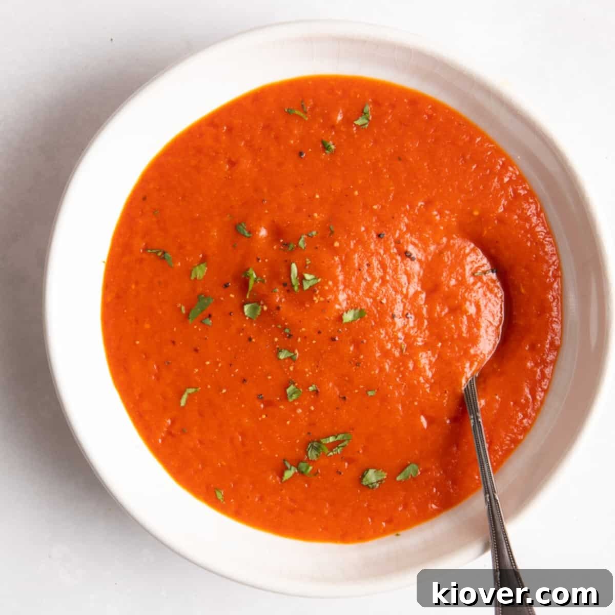 Red Pepper & Tomato Soup served in a white bowl with a spoon on a white background.