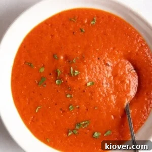 red pepper and tomato soup served in a white bowl with a spoon inside.