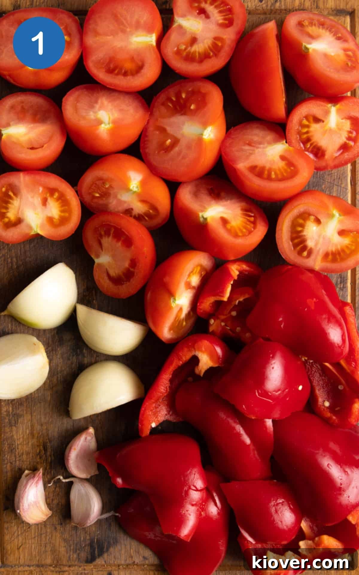 chopped tomatoes, pepper, onion and garlic on a wooden chopping board.