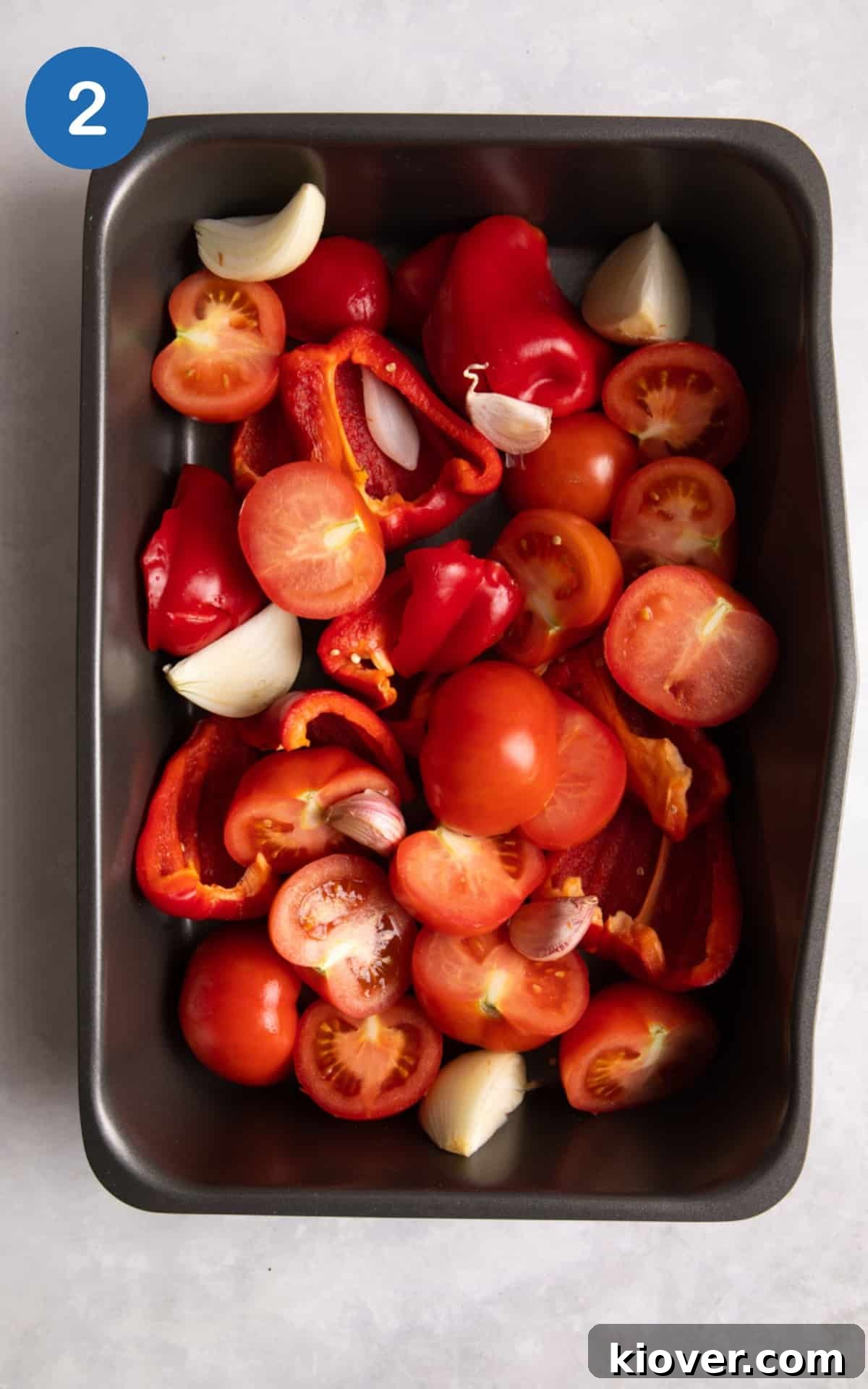 tomatoes, pepper, onion and garlic all in a silver baking tray ready to bake.