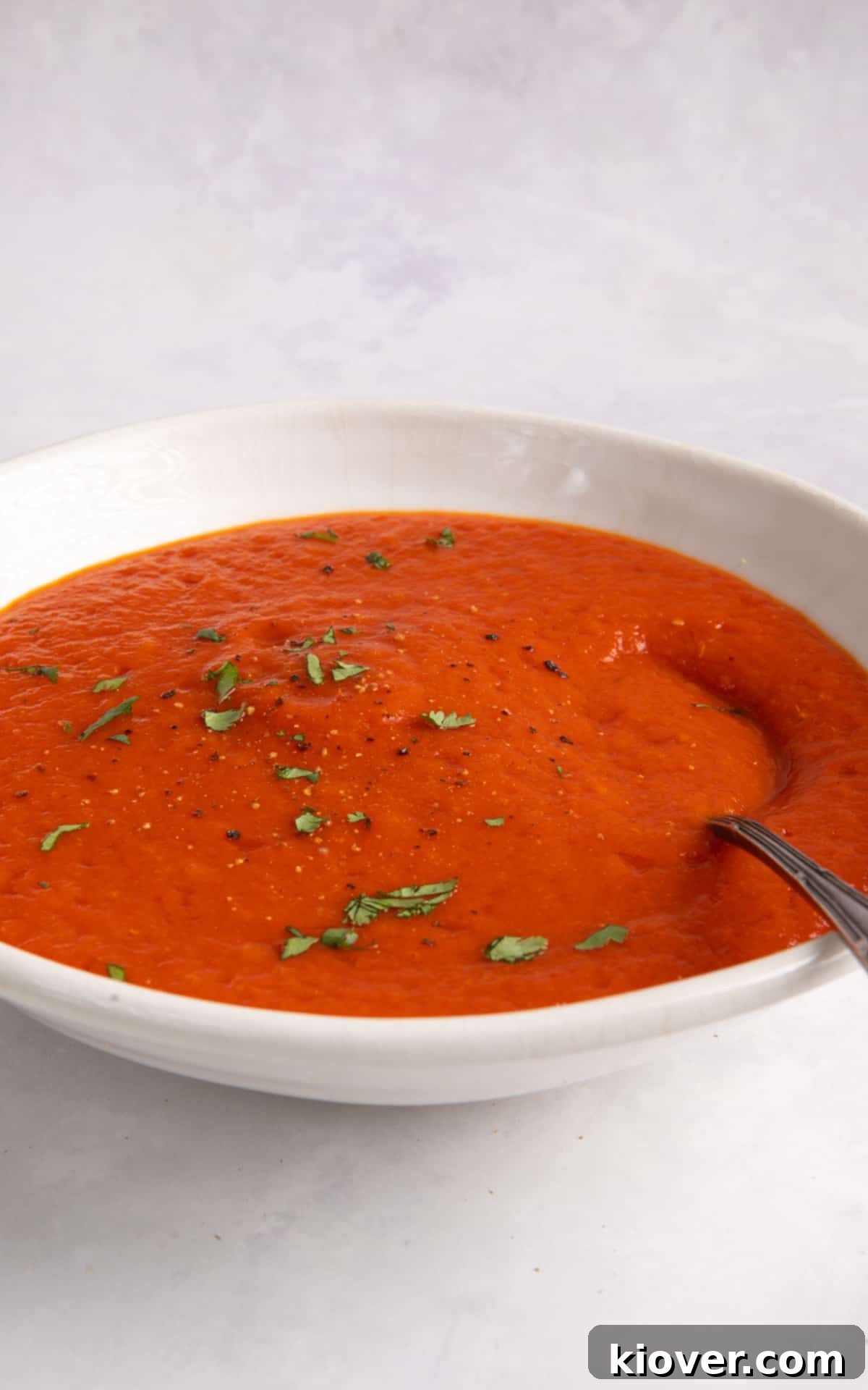roasted red pepper and tomato soup served in a white bowl with a spoon.