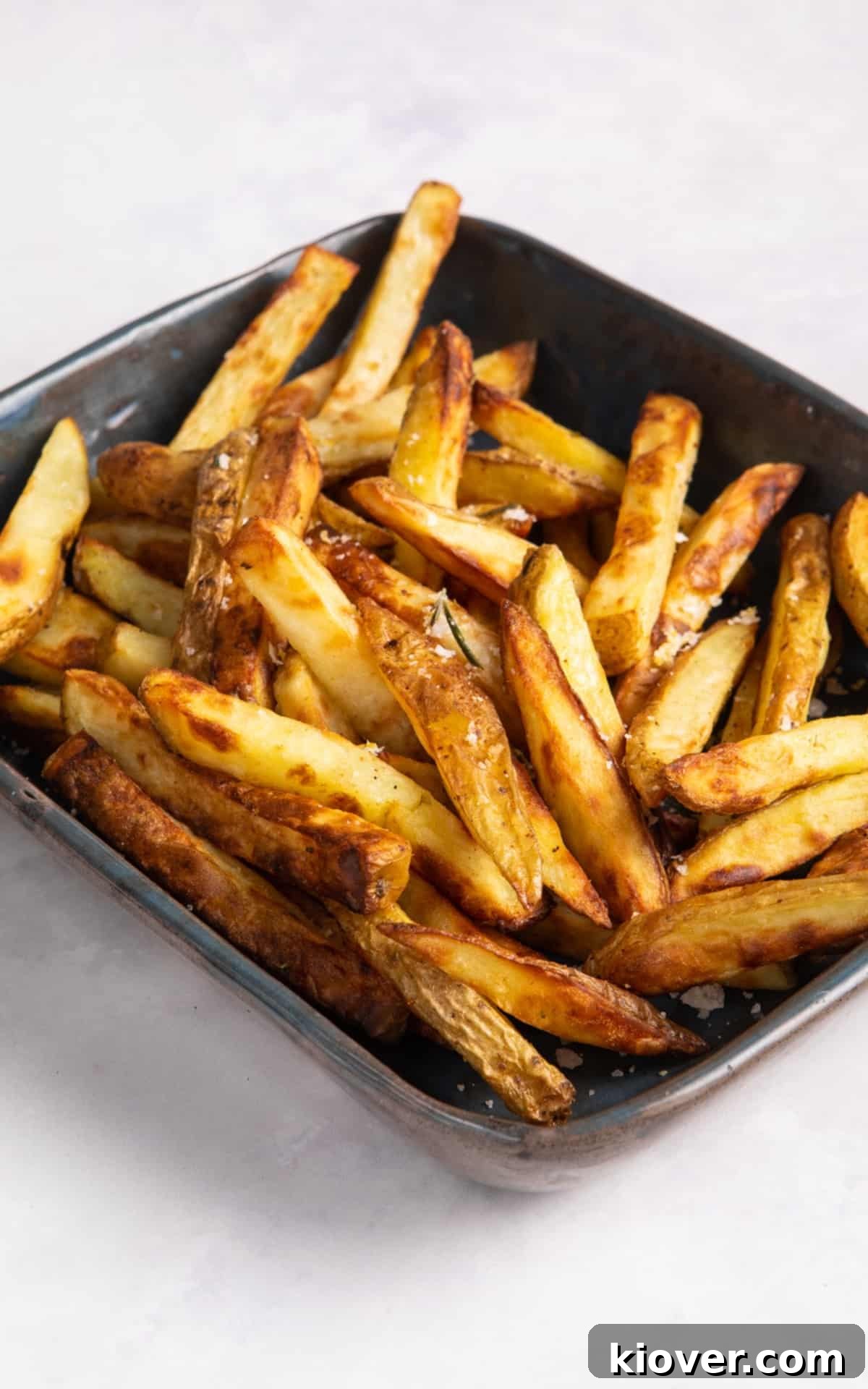 Crispy Air Fryer French Fries: Quick Homemade Recipe 7 Air fryer chips in dark coloured rectangular dish. Dish is on white surface.