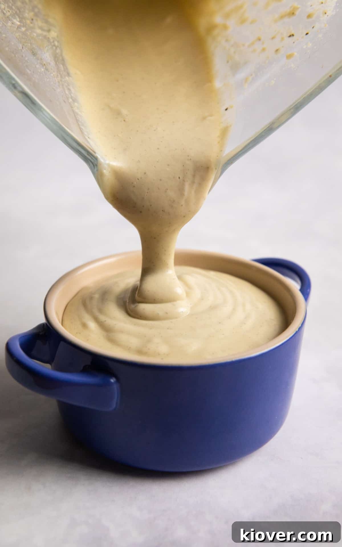 Creamy Vegan Béchamel Sauce Recipe for Pasta & Lasagna 6 white sauce being poured from blender into small dish on white surface.