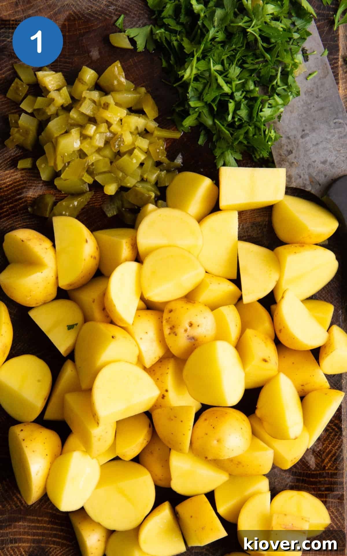 chopped new potatoes, gherkins and parsley on dark wooden chopping board with knife.