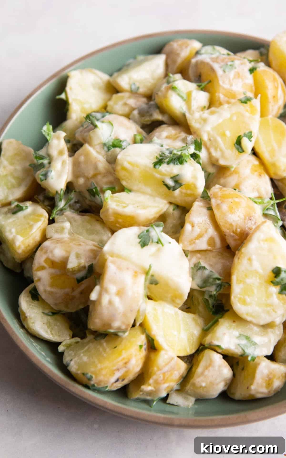 potato salad in green bowl with beige rim. Bowl is on white surface.
