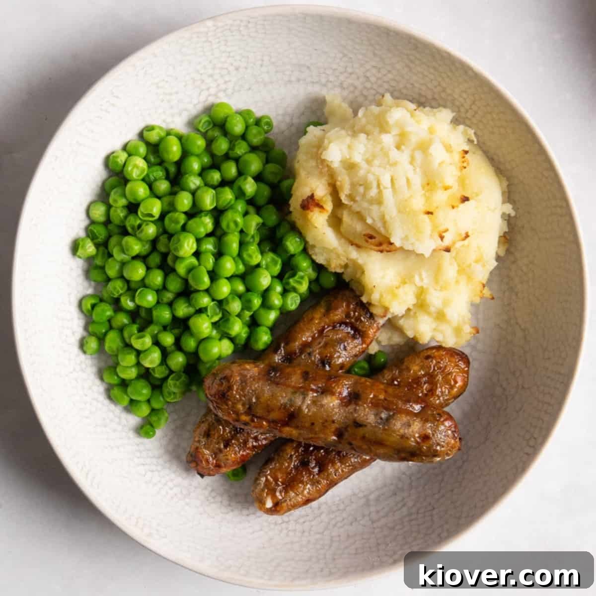air fryer sausages in a bowl served with mash potato and peas.