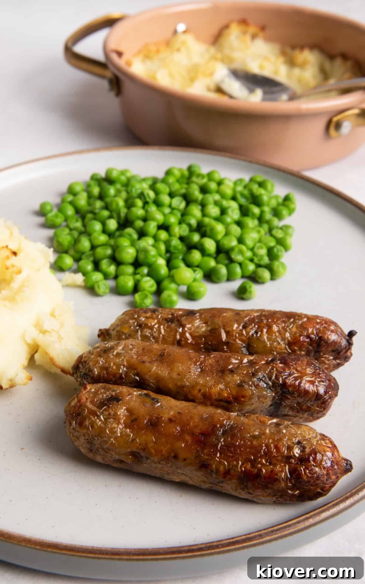 3 sausages on grey plate with peas and mashed potato.