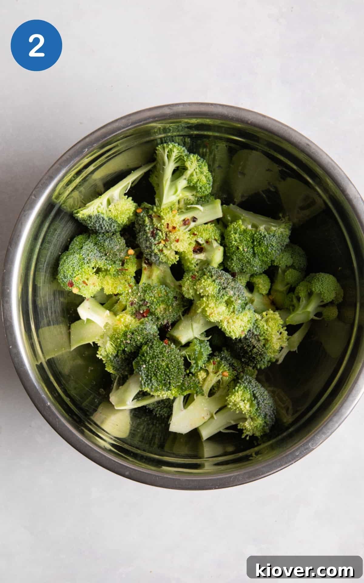 Crispy Air Fryer Broccoli Recipe — Quick Dinner Side 5 broccoli in large silver mixing bowl. Bowl is on white surface.