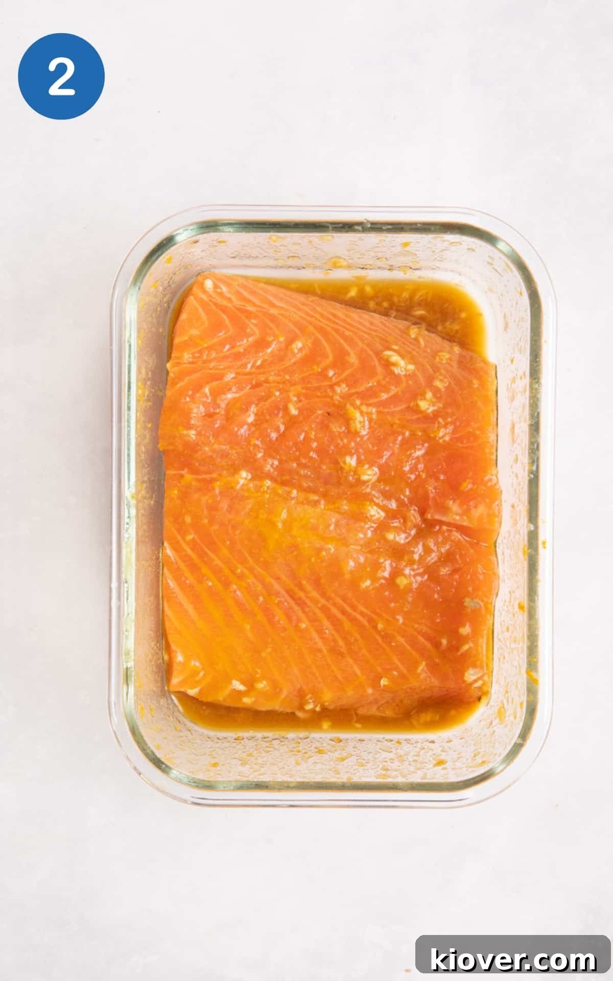 marinaded salmon fillets in transparent container on white surface.
