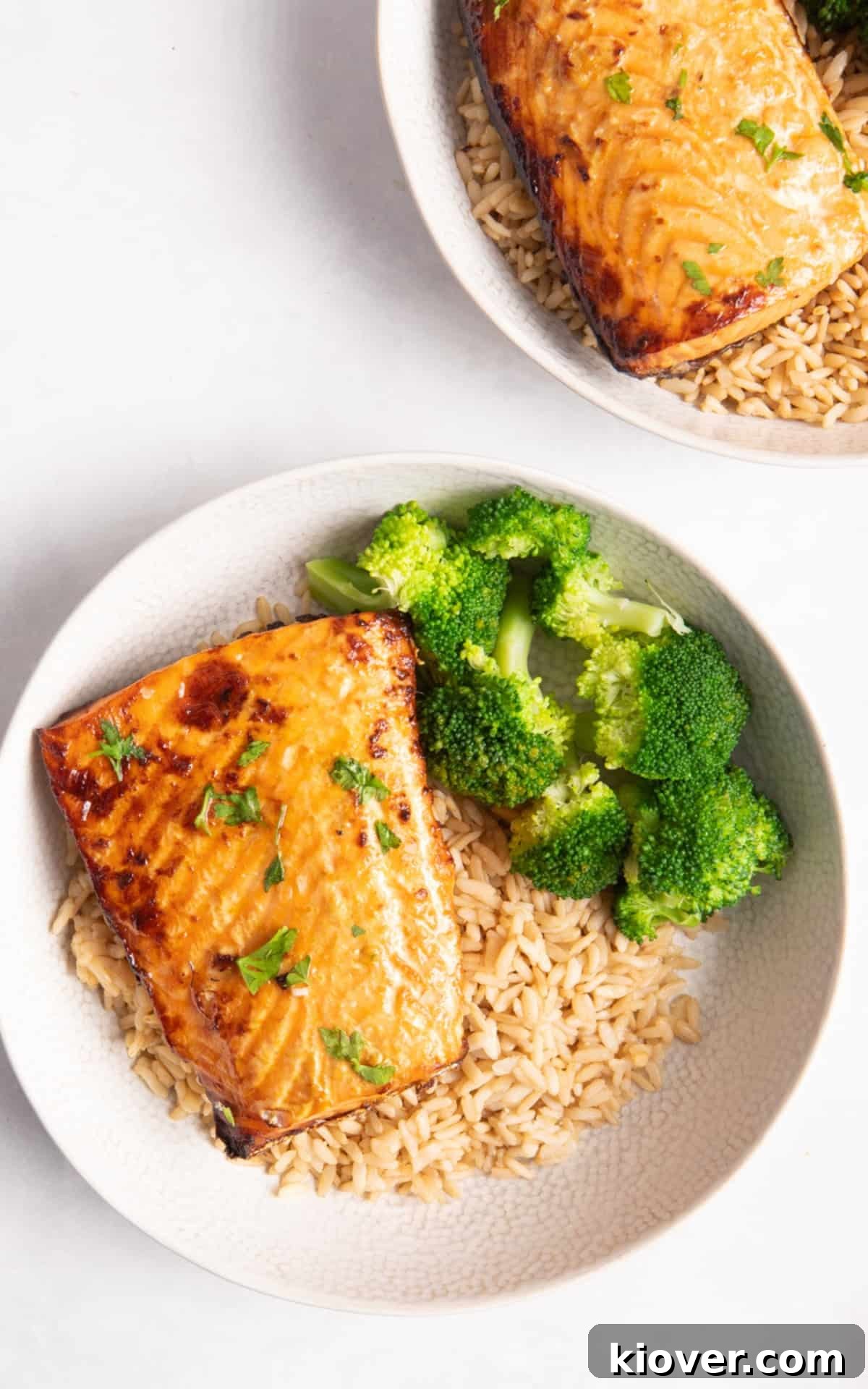 salmon fillets in bowls with rice and broccoli on white surface.