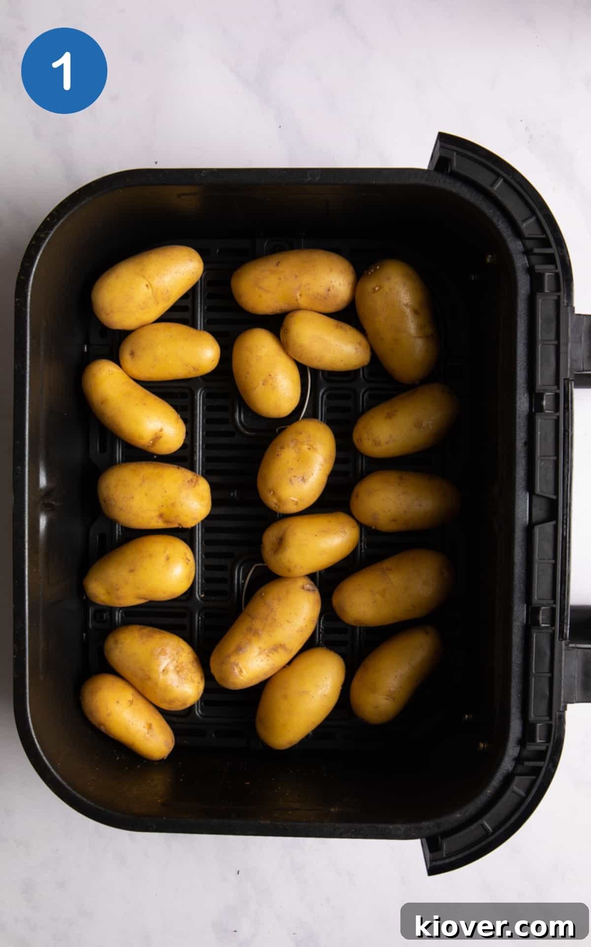 Crispy Air Fryer Smashed Potatoes with Garlic and Parmesan 4 Raw new potatoes in air fryer tray on white surface.