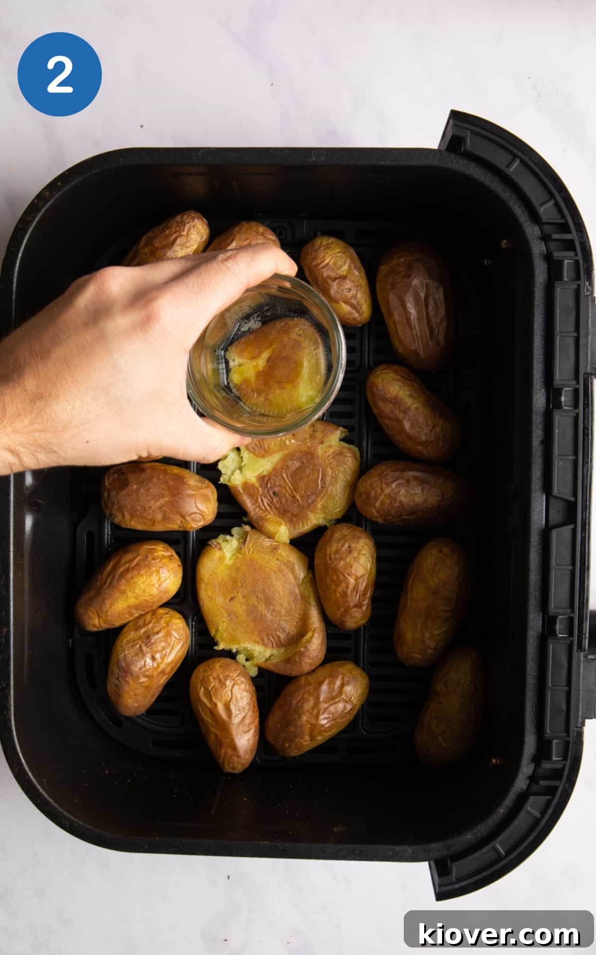 Crispy Air Fryer Smashed Potatoes with Garlic and Parmesan 5 New potatoes in air fryer tray being squashed with glass jar.