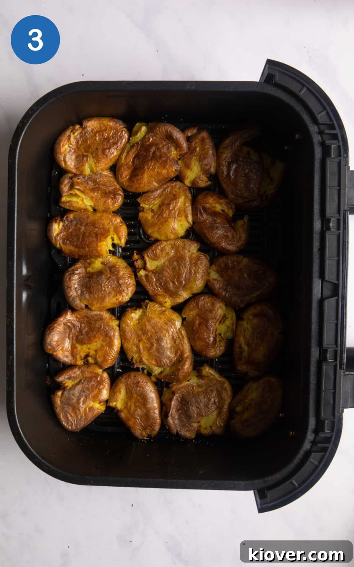 Crispy Air Fryer Smashed Potatoes with Garlic and Parmesan 6 crushed new potatoes drizzled with olive oil and sea salt in air fryer tray. tray is on white background.