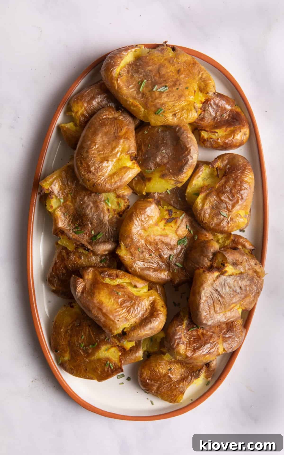 Crispy Air Fryer Smashed Potatoes with Garlic and Parmesan 7 Overhead shot of air fryer roast potatoes on white plate with orange rim. The plate is on white marble background.