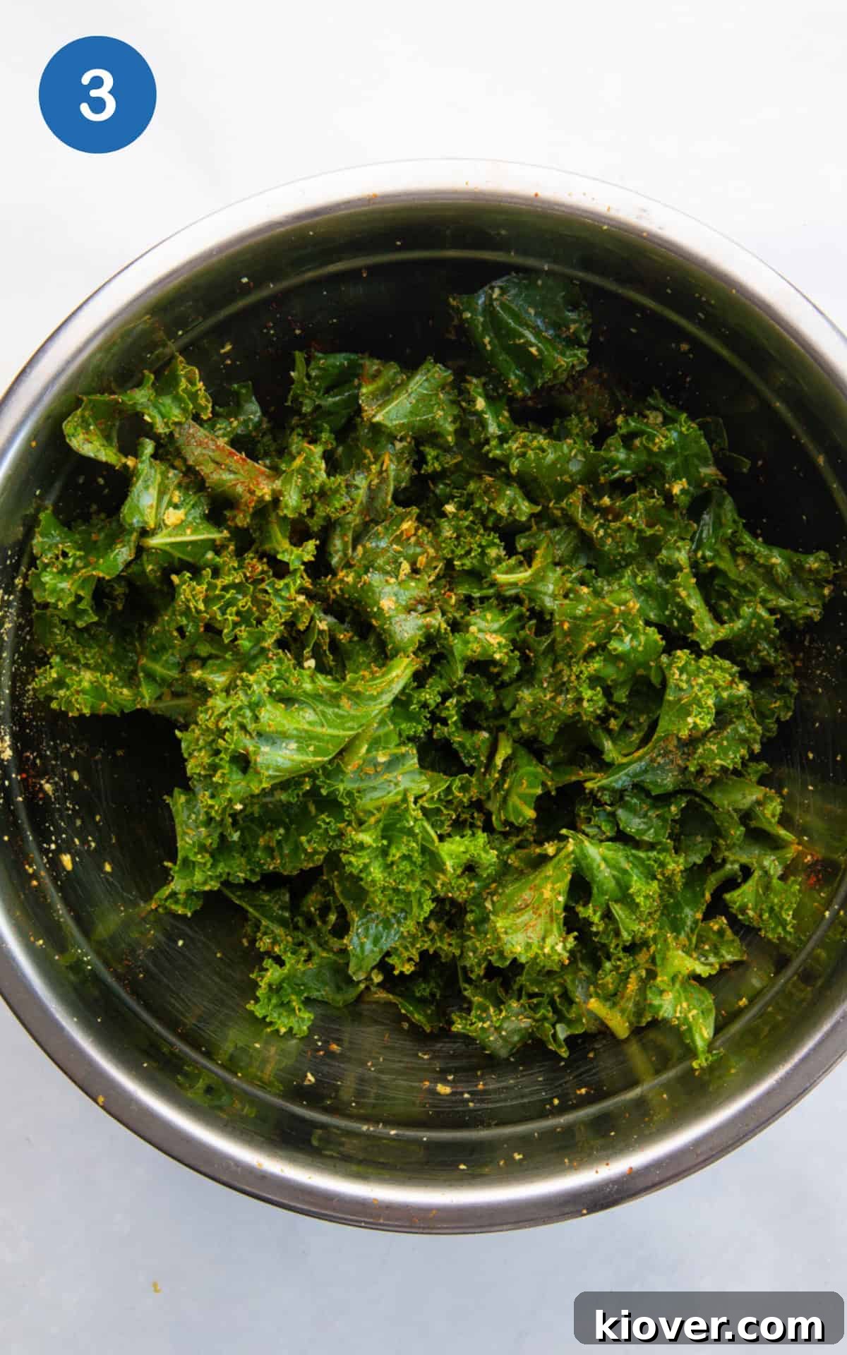 adding seasonings to the kale in a bowl.