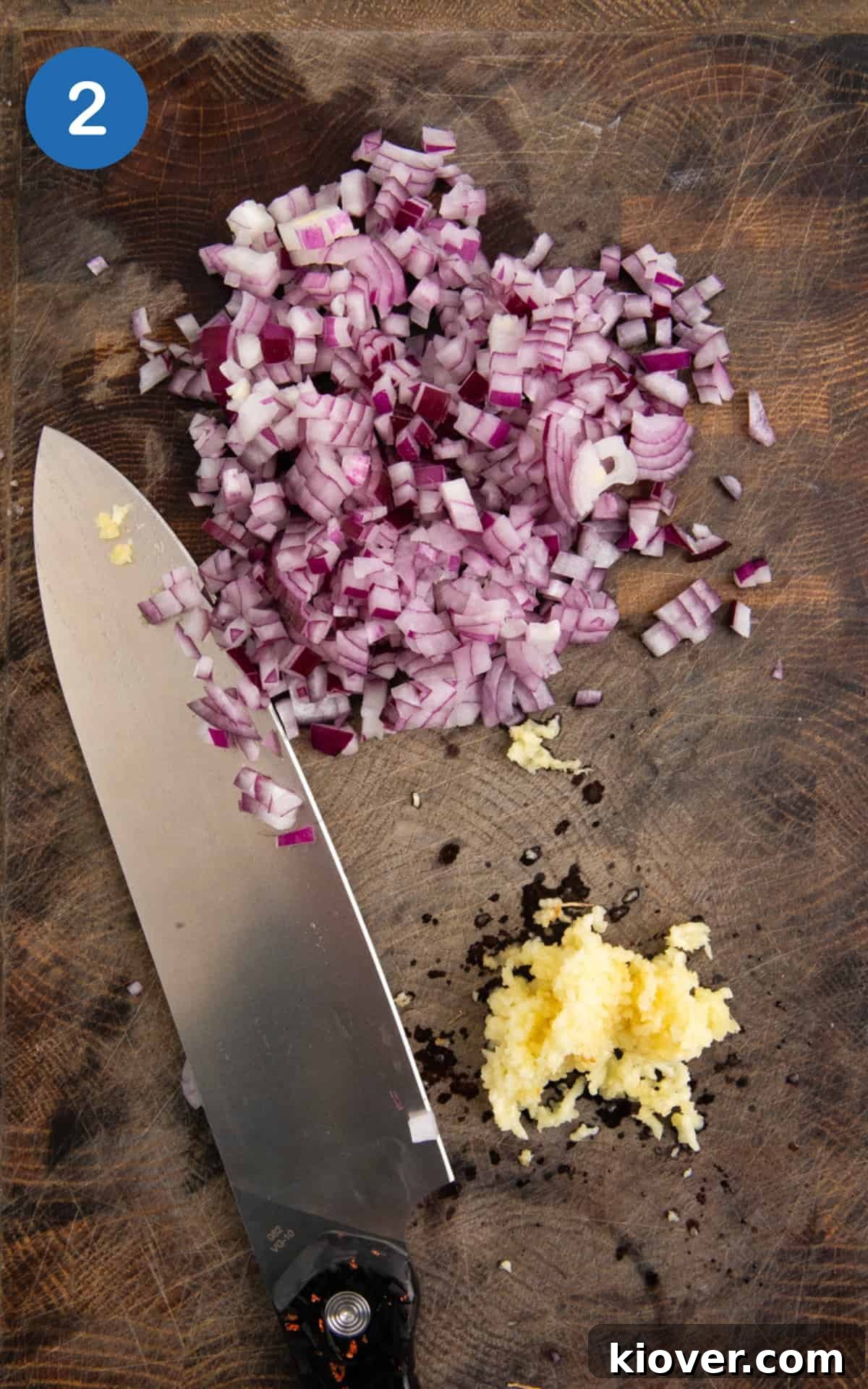 diced red onion and crushed garlic on a wooden chopping board with large knife.