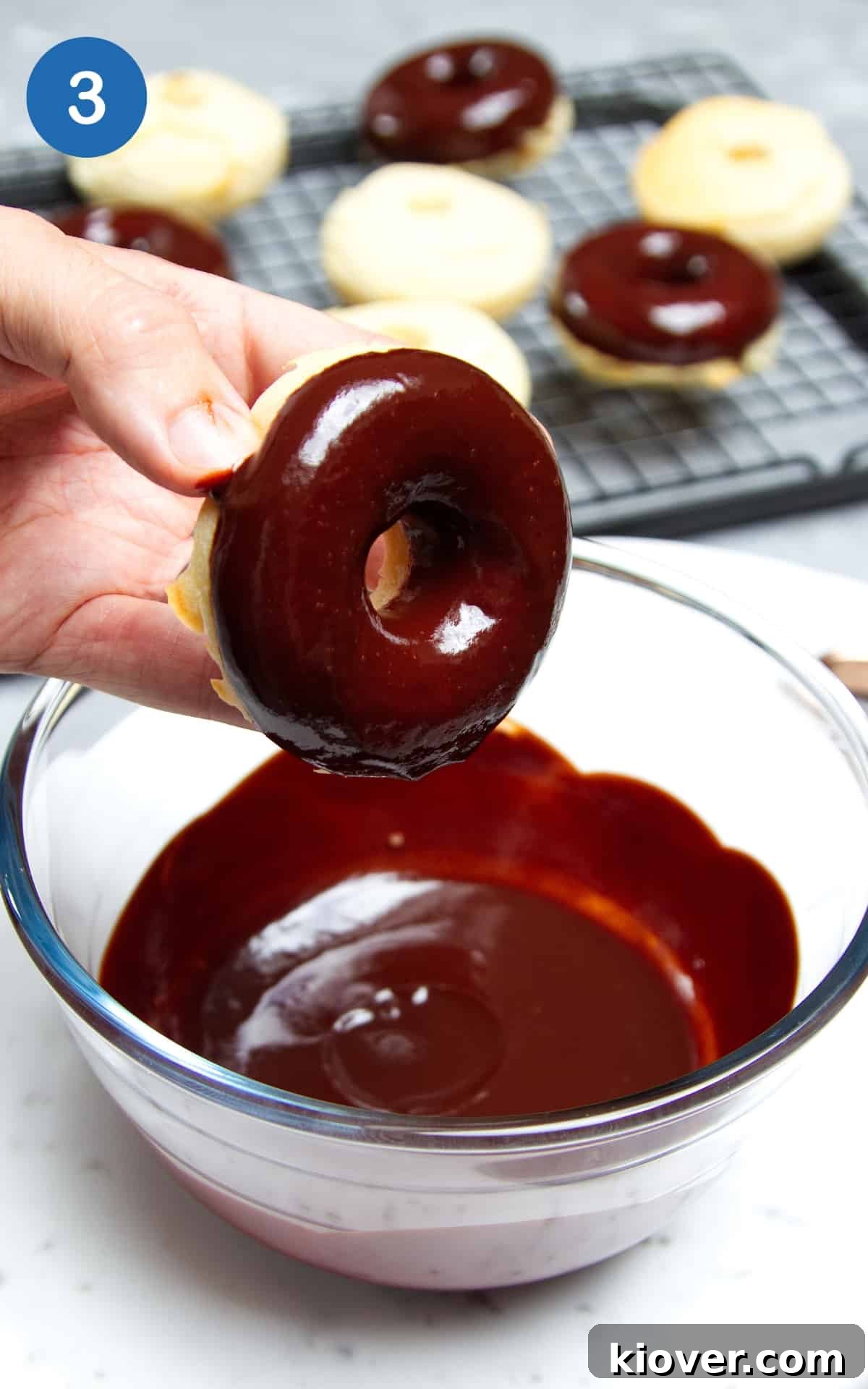 doughnuts being dipped into a bowl of chocolate sauce.