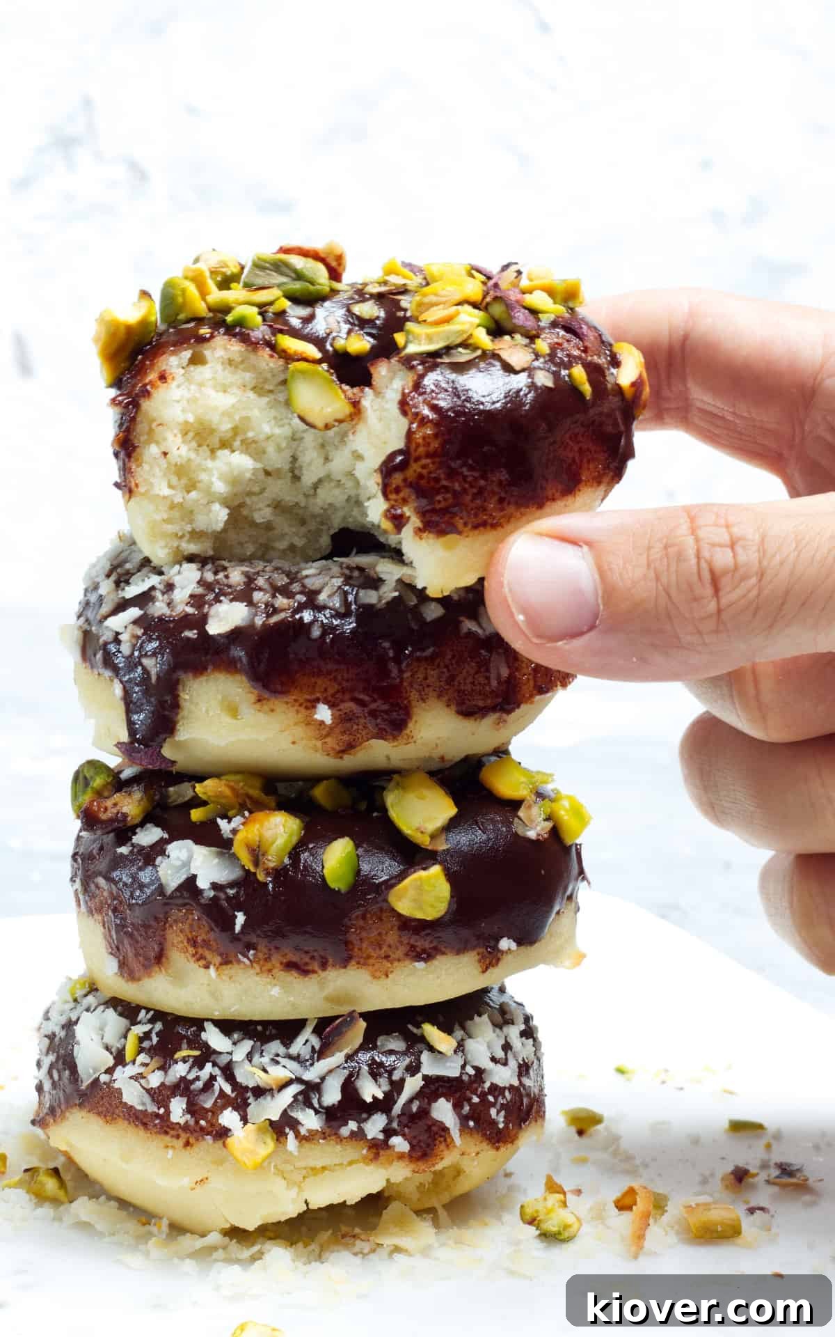 stacked doughnuts on white plate with bite taken out.