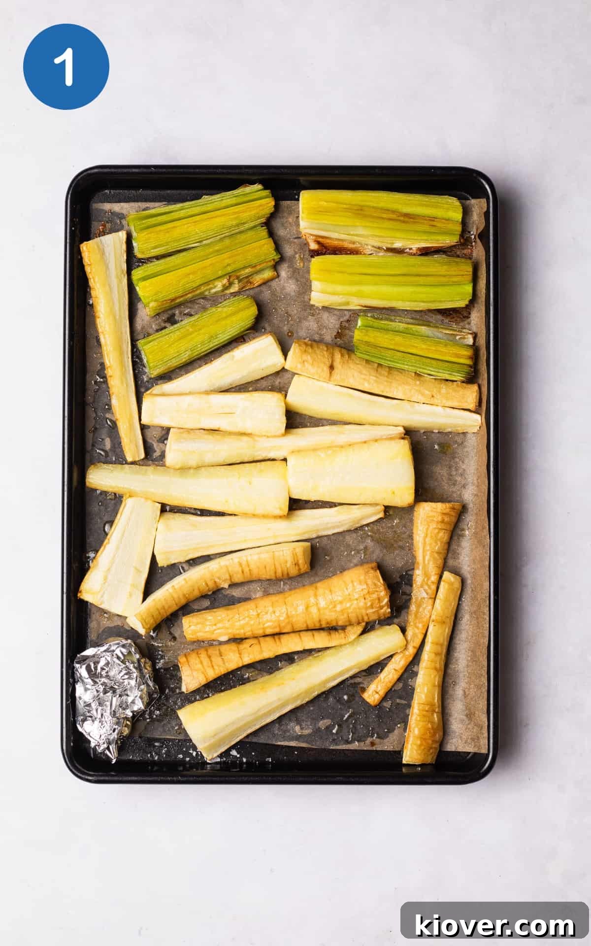 Creamy Roasted Parsnip Soup Recipe with Garlic and Thyme 4 chopped leek and parsnips on a lined baking tray with garlic cloves in a tin foil.